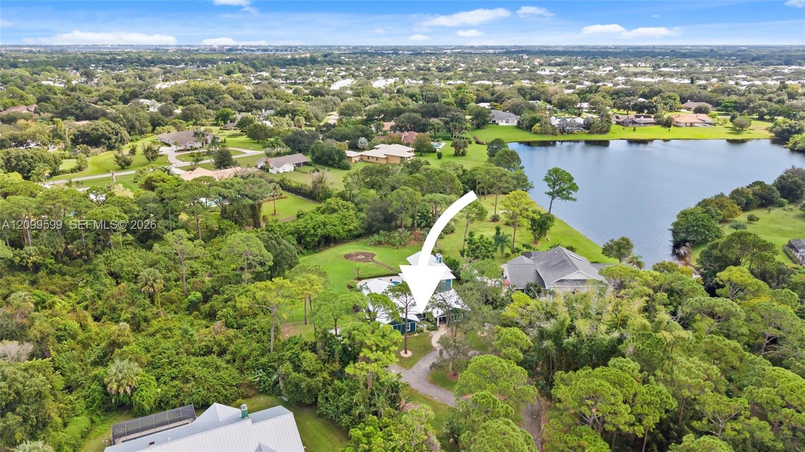 Aerial perspective featuring a multi-story residence situated on a landscaped lot with mature trees and proximity to a lake