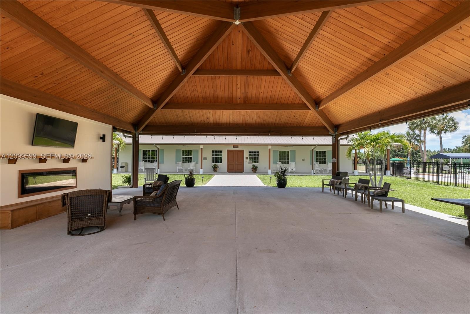 Expansive covered patio featuring a vaulted wood-plank ceiling, exposed timber trusses, concrete flooring, and a built-in linear electric fireplace