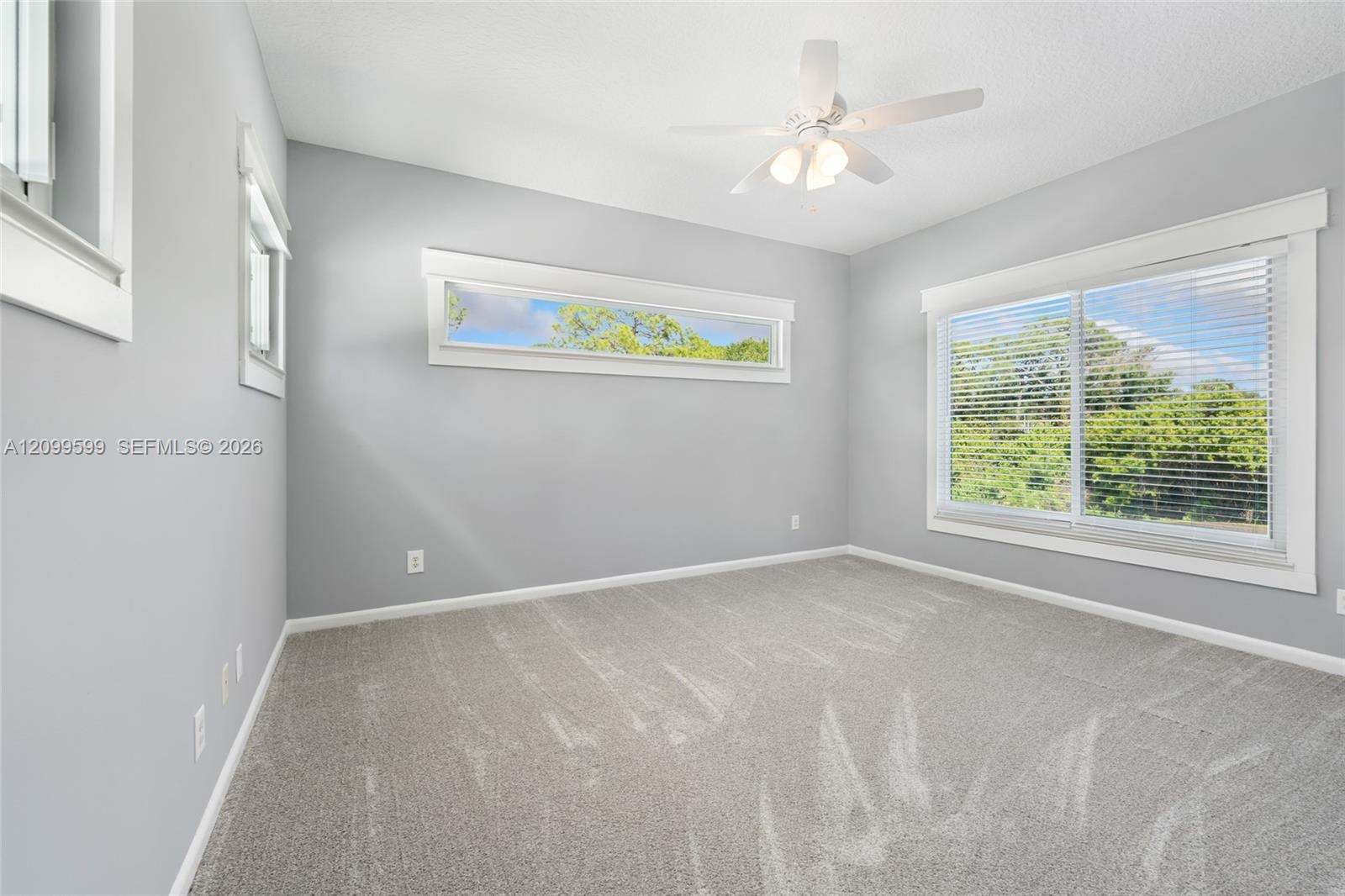 Neutral-toned walls with high-set horizontal windows, a large multi-pane window, wall-to-wall carpeting, and a ceiling-mounted fan with integrated lig