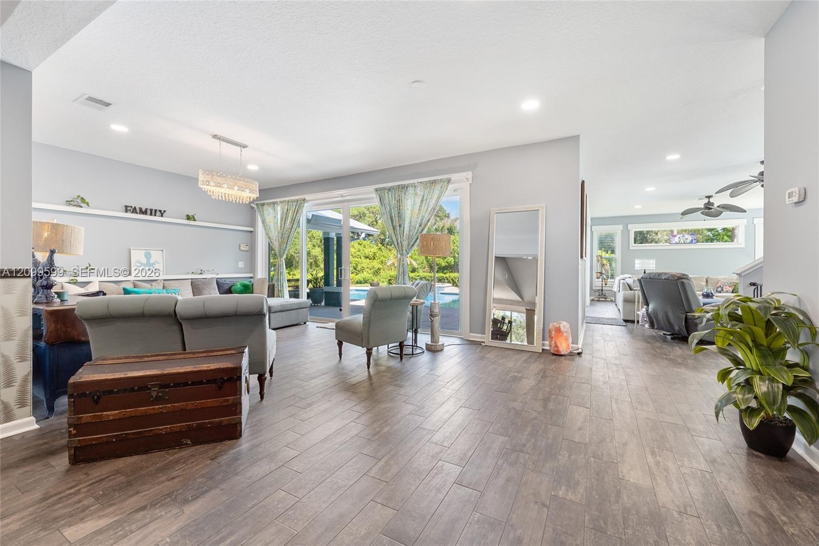 Open-concept living space featuring wood-finish flooring, recessed lighting, a statement crystal chandelier, and sliding glass doors