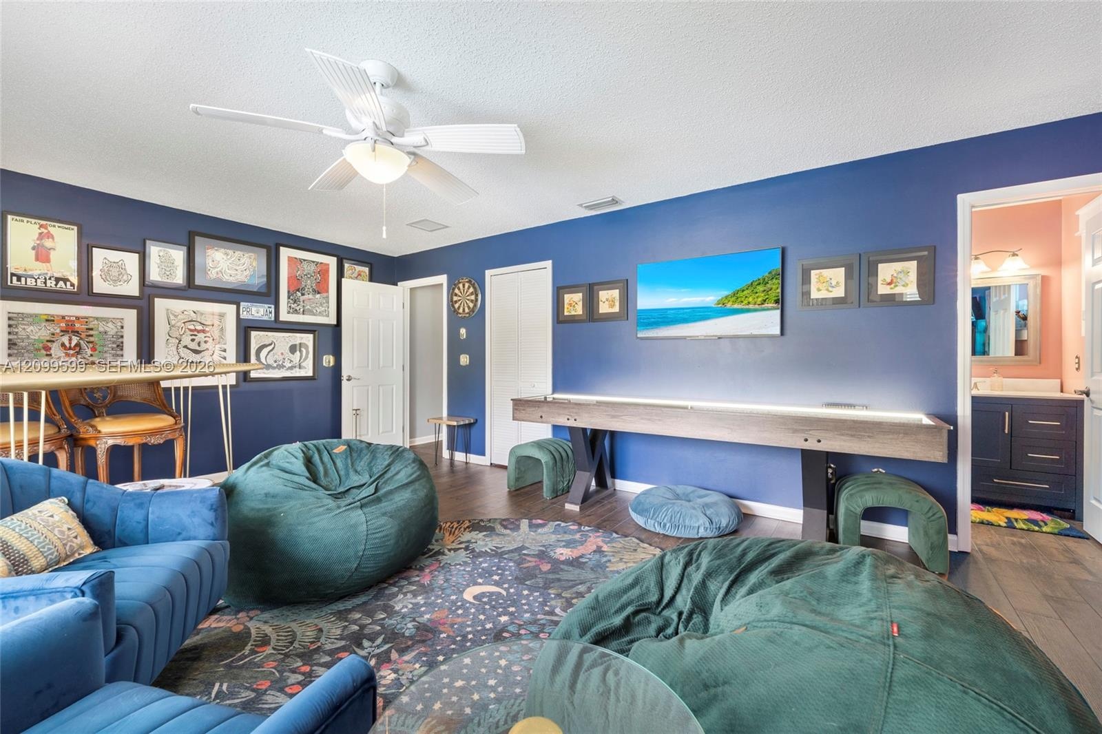 Spacious room featuring wood-finish flooring, a ceiling fan with integrated lighting, and multiple interior doors