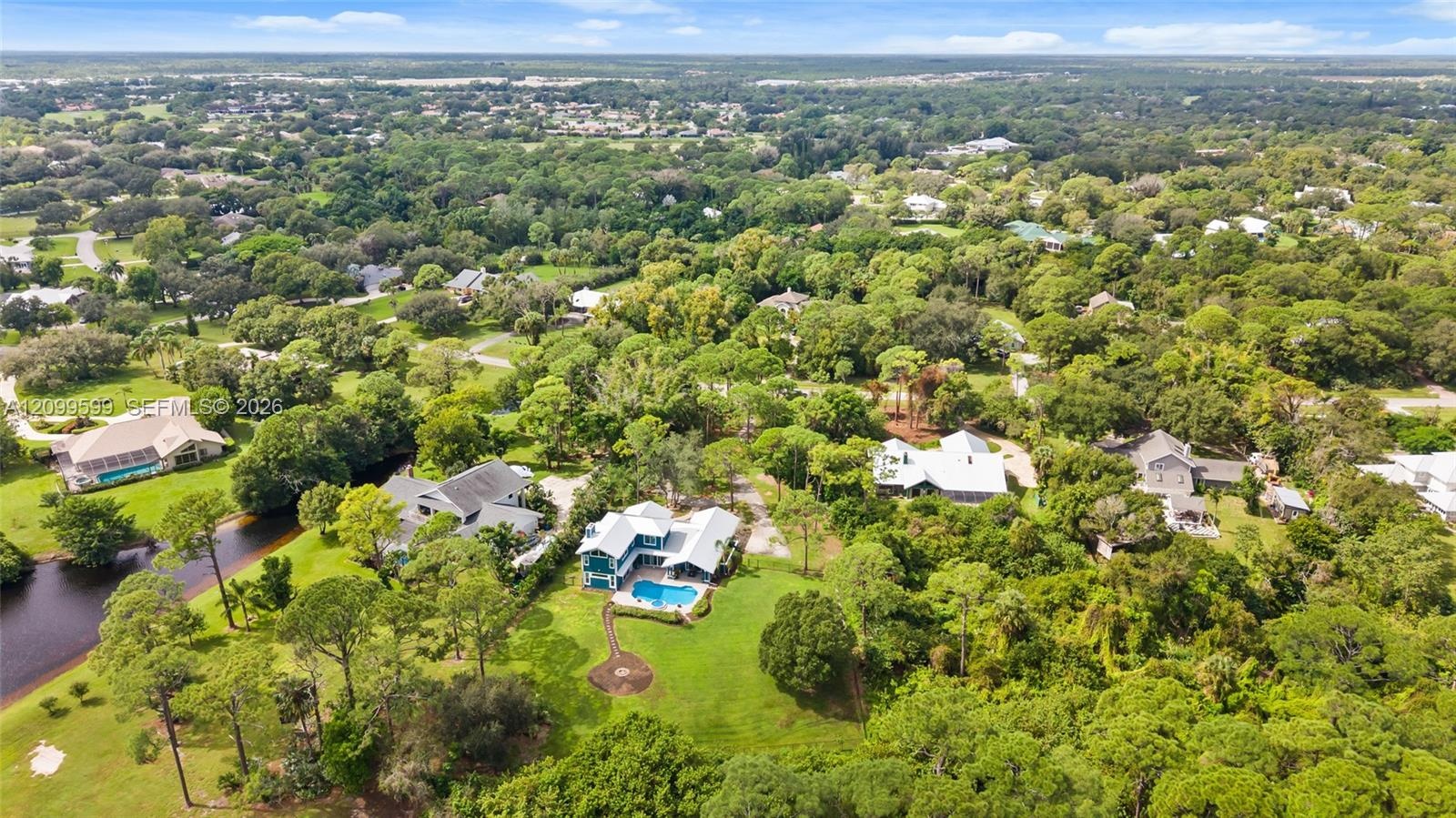 Aerial perspective featuring a multi-story residence with a metal roof, an in-ground swimming pool, a stone-paved patio, and established mature trees 