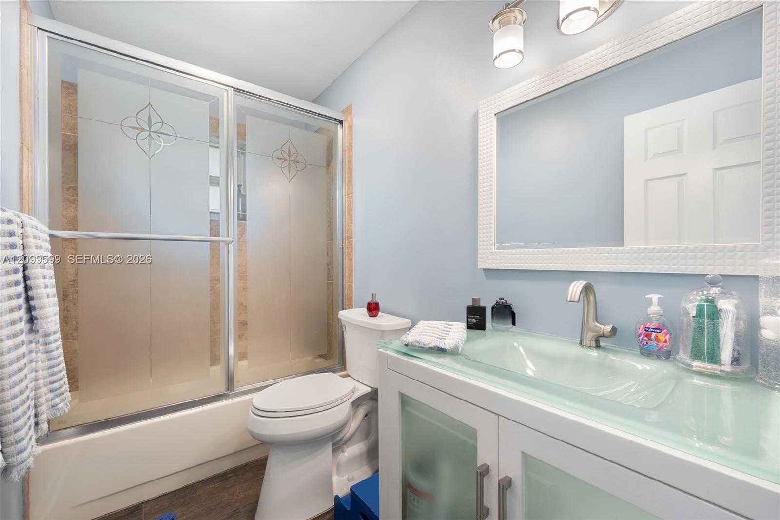 Bathroom featuring a vanity with an integrated glass sink and countertop, frosted glass cabinet inserts, a shower enclosure with decorative etched gla