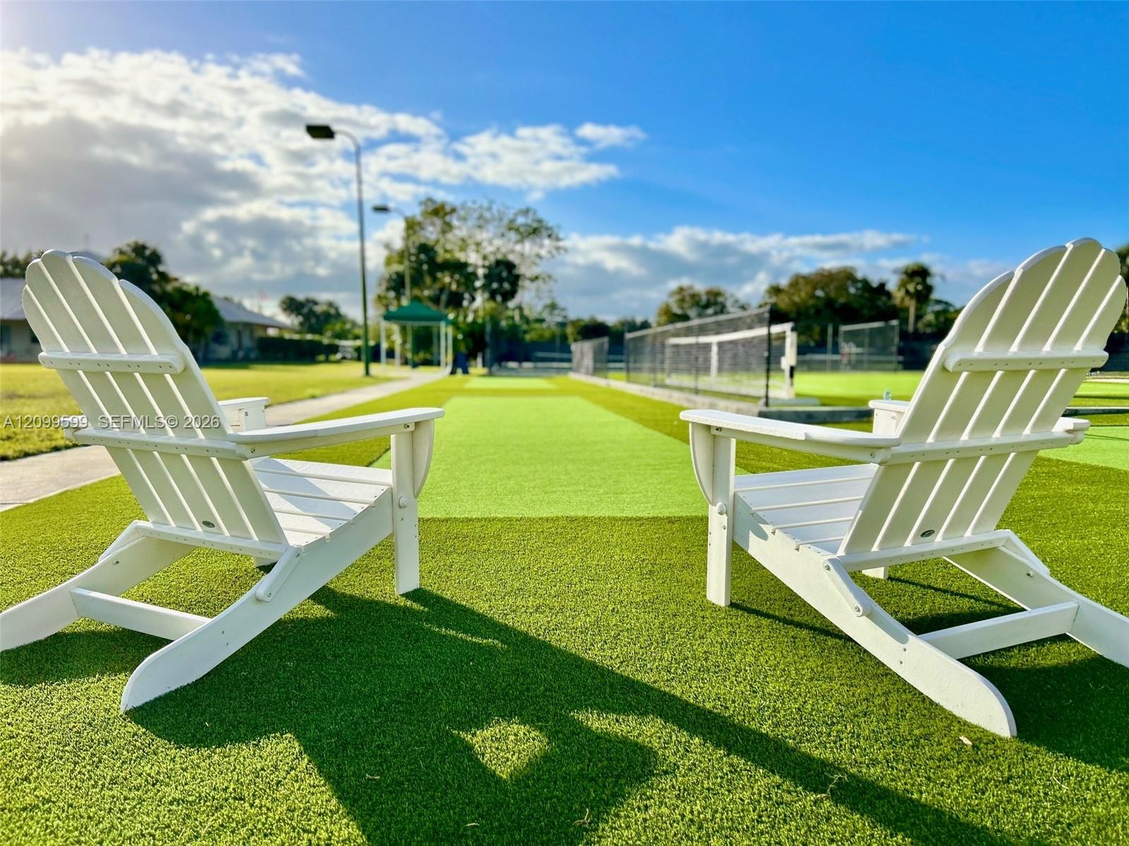 Synthetic turf recreational area featuring a multi-sport court with perimeter fencing and tall exterior lighting