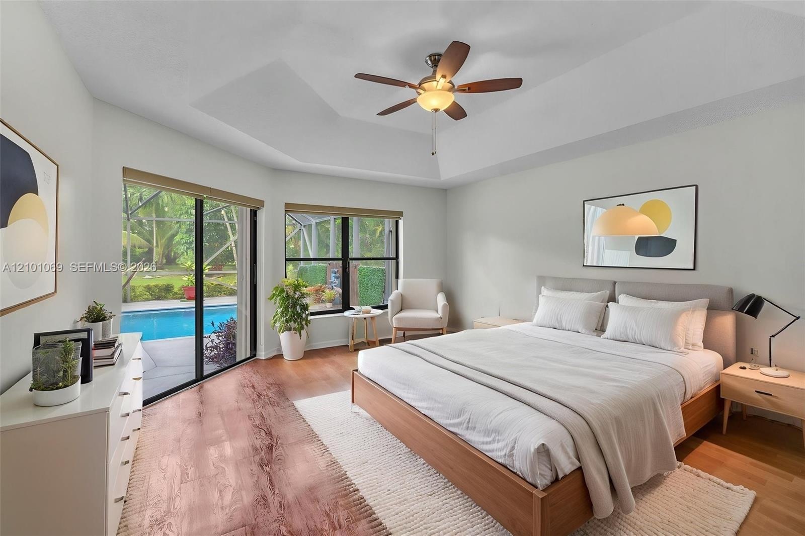 Master bedroom, tray ceiling, wood-finish flooring, and large sliding glass doors providing outdoor access-virtually staged