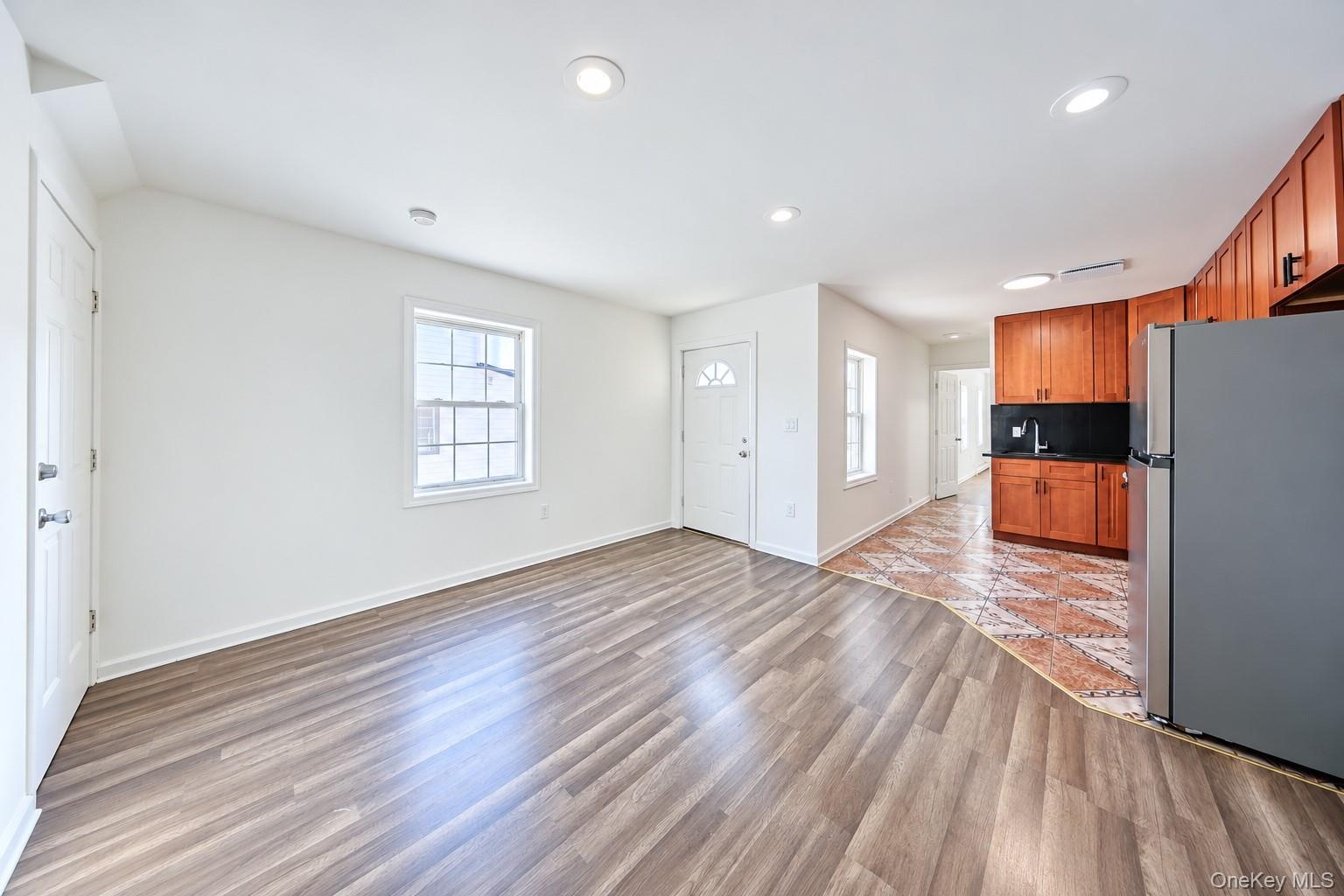 Wood-finish flooring, recessed lighting, wood cabinetry, patterned tile flooring, and a stainless steel refrigerator