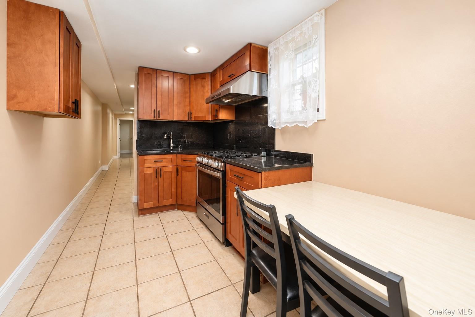 Kitchen featuring wood cabinetry, stone countertops, stainless steel gas range, stainless steel range hood, and tile flooring