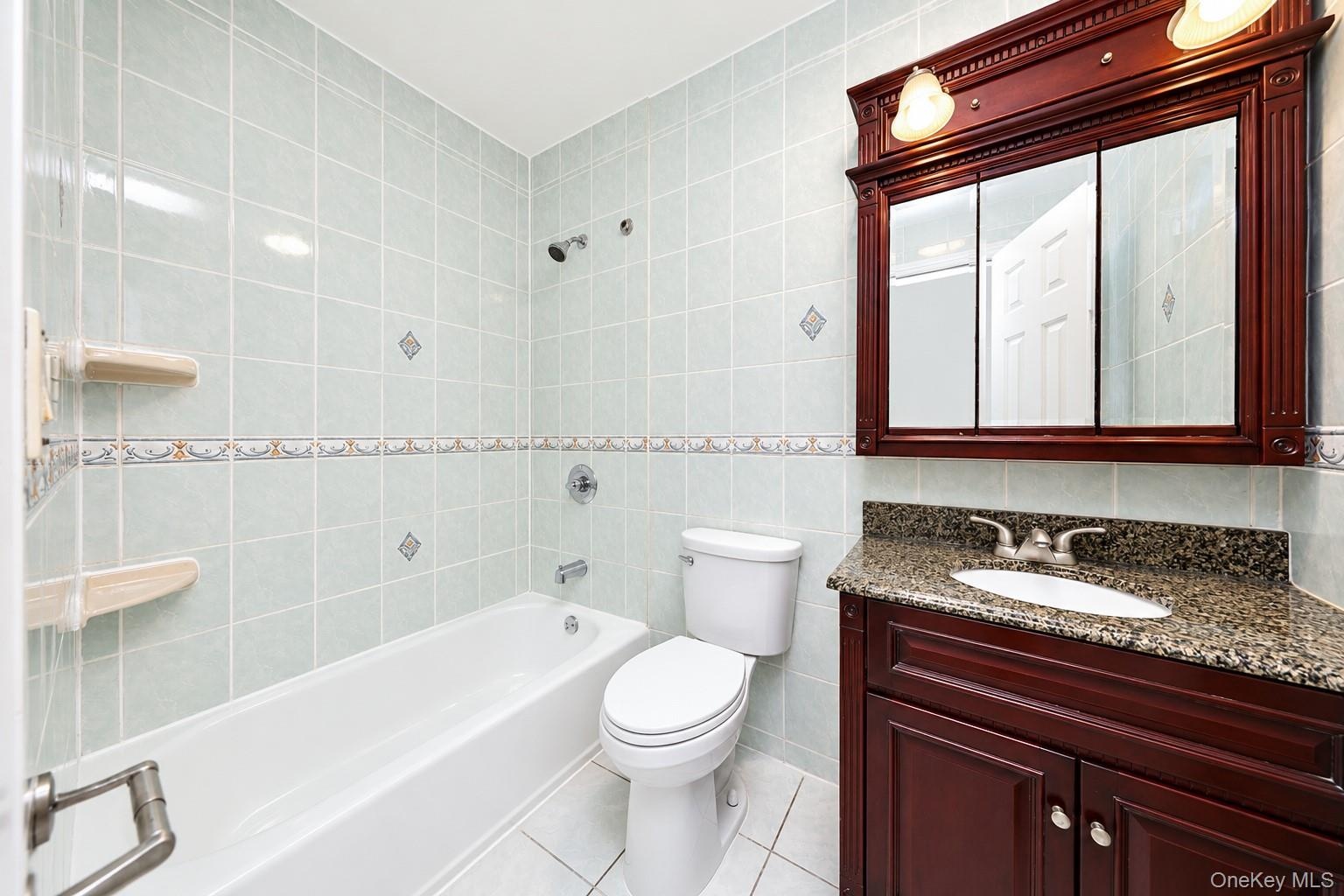 Bathroom featuring a vanity with stone-finish countertop, decorative tile surround, built-in medicine cabinet with integrated lighting, and a bathtub 