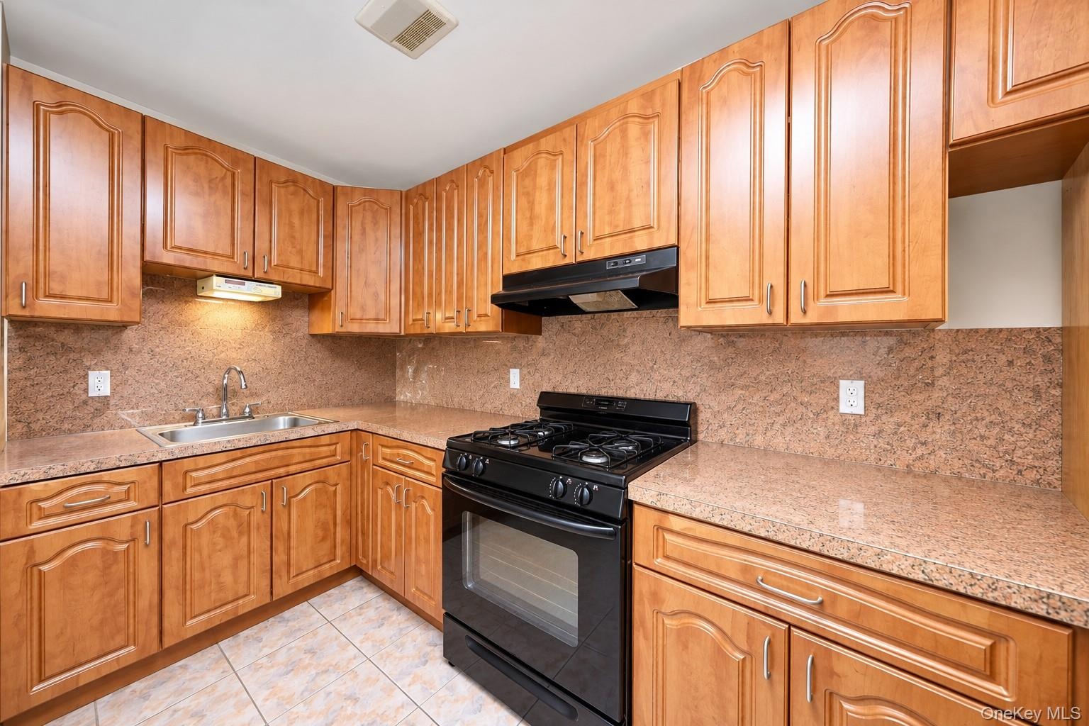 Kitchen featuring wood cabinetry, stone-surface countertops, full-height stone backsplash, under-cabinet lighting, and integrated black gas range