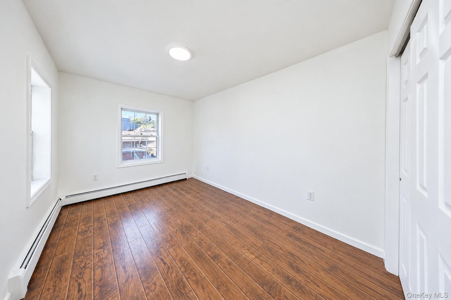 Interior room featuring wood-finish flooring, white walls, dual-pane windows, and a sliding-door closet