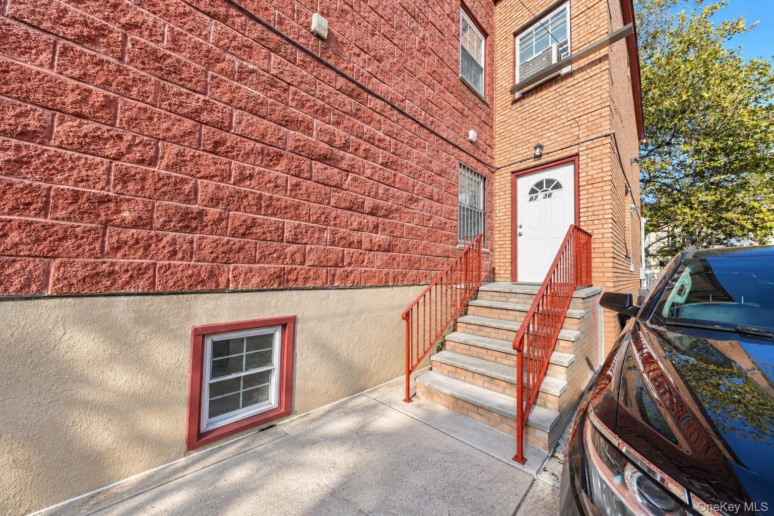 Exterior featuring red textured masonry, tan stucco lower siding, concrete staircase with metal railings, and white entry door with arched transom win