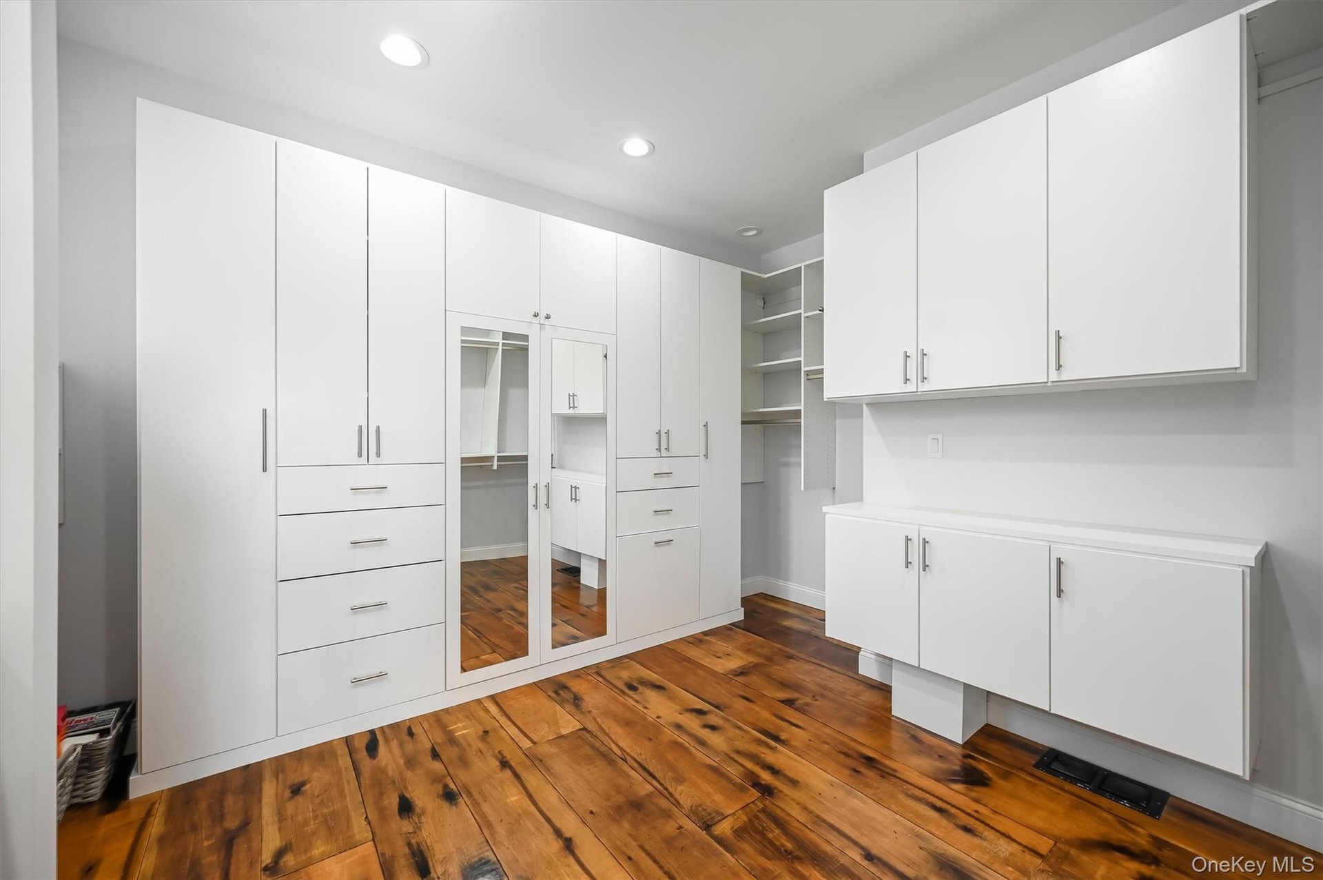 Custom floor-to-ceiling white cabinetry with integrated drawer storage, mirrored paneling, open shelving, and wood-finish flooring