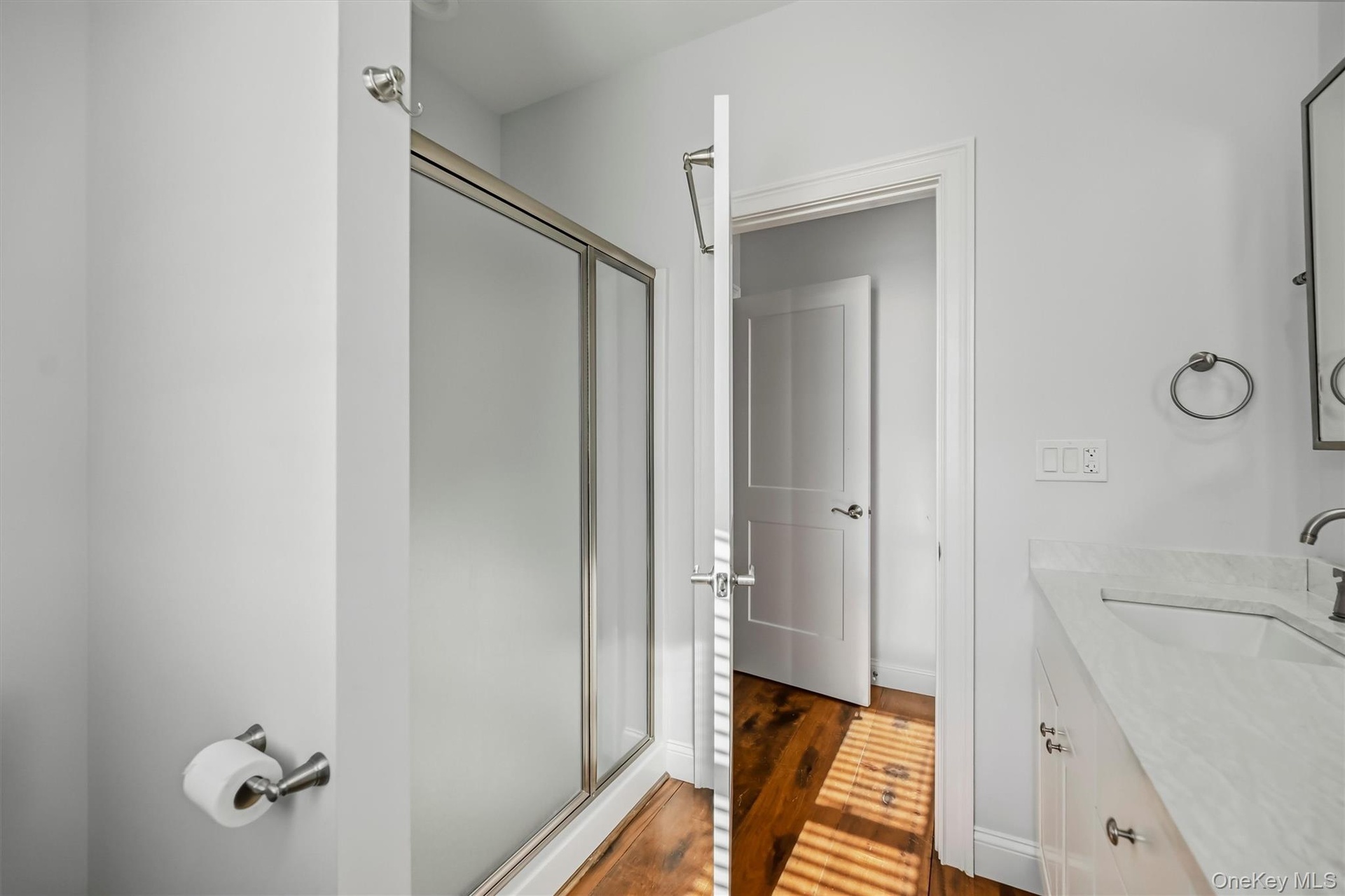 Shower enclosure with a metal frame, vanity featuring a stone countertop with an integrated sink, metal wall-mounted hardware, and wood-finish floorin