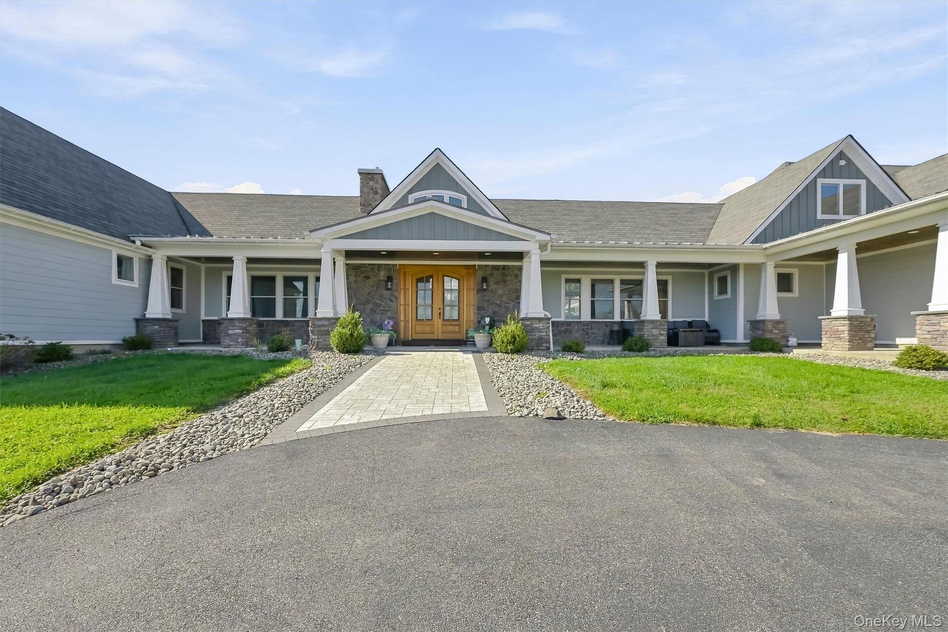 Exterior featuring a horizontal siding facade, stone masonry accents, a covered front porch with white columns, a paved walkway, and double wood-finis