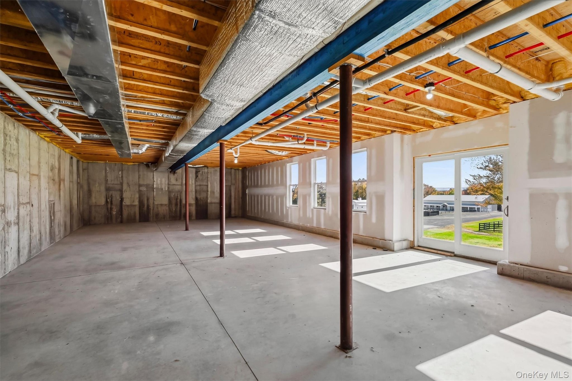 Unfinished space featuring exposed timber joist ceiling, concrete flooring, concrete foundation walls, structural support columns, and sliding glass e