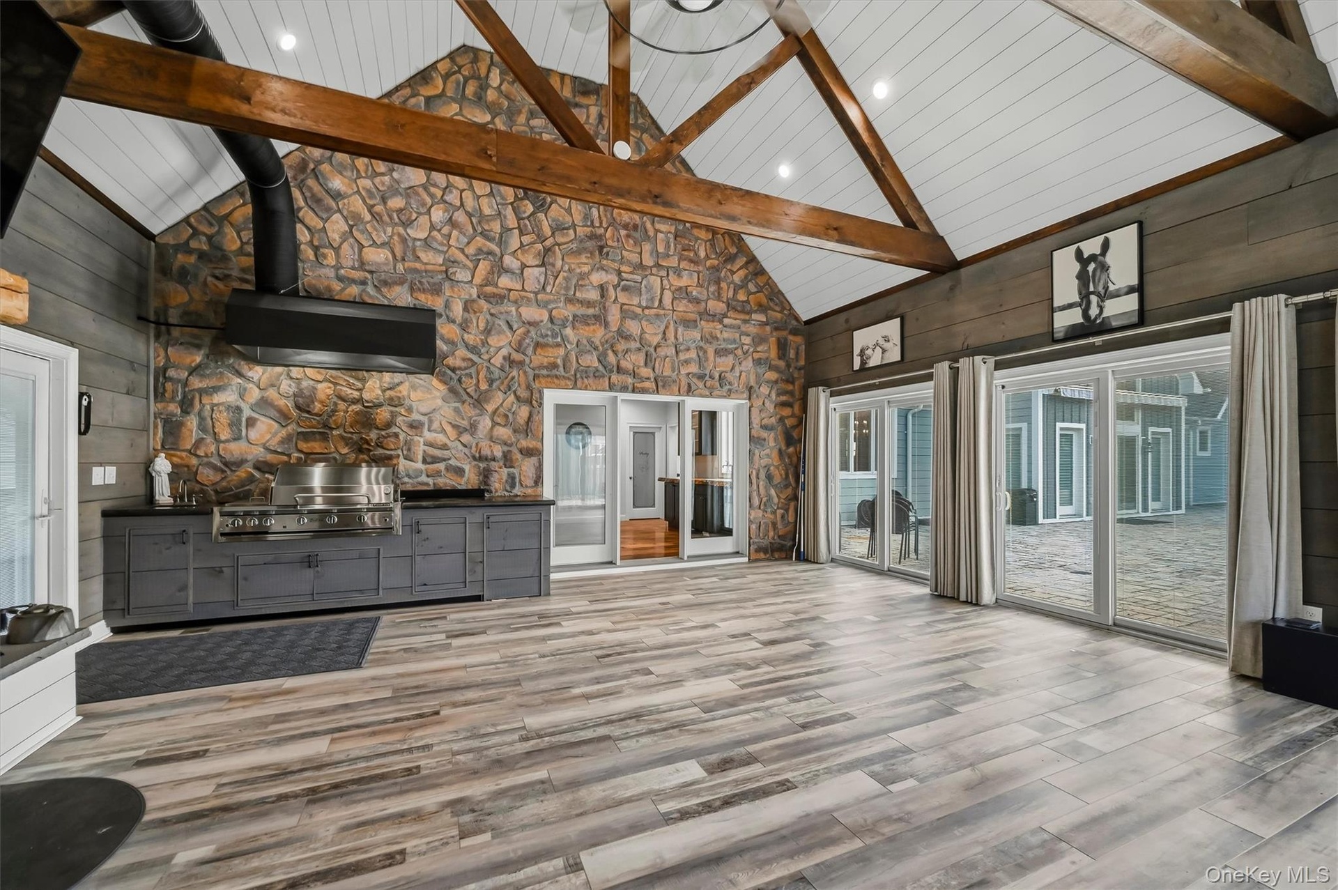 Vaulted ceilings with exposed timber trusses, stone accent wall, wood-finish flooring, built-in cabinetry with stainless steel grill, and glass slidin