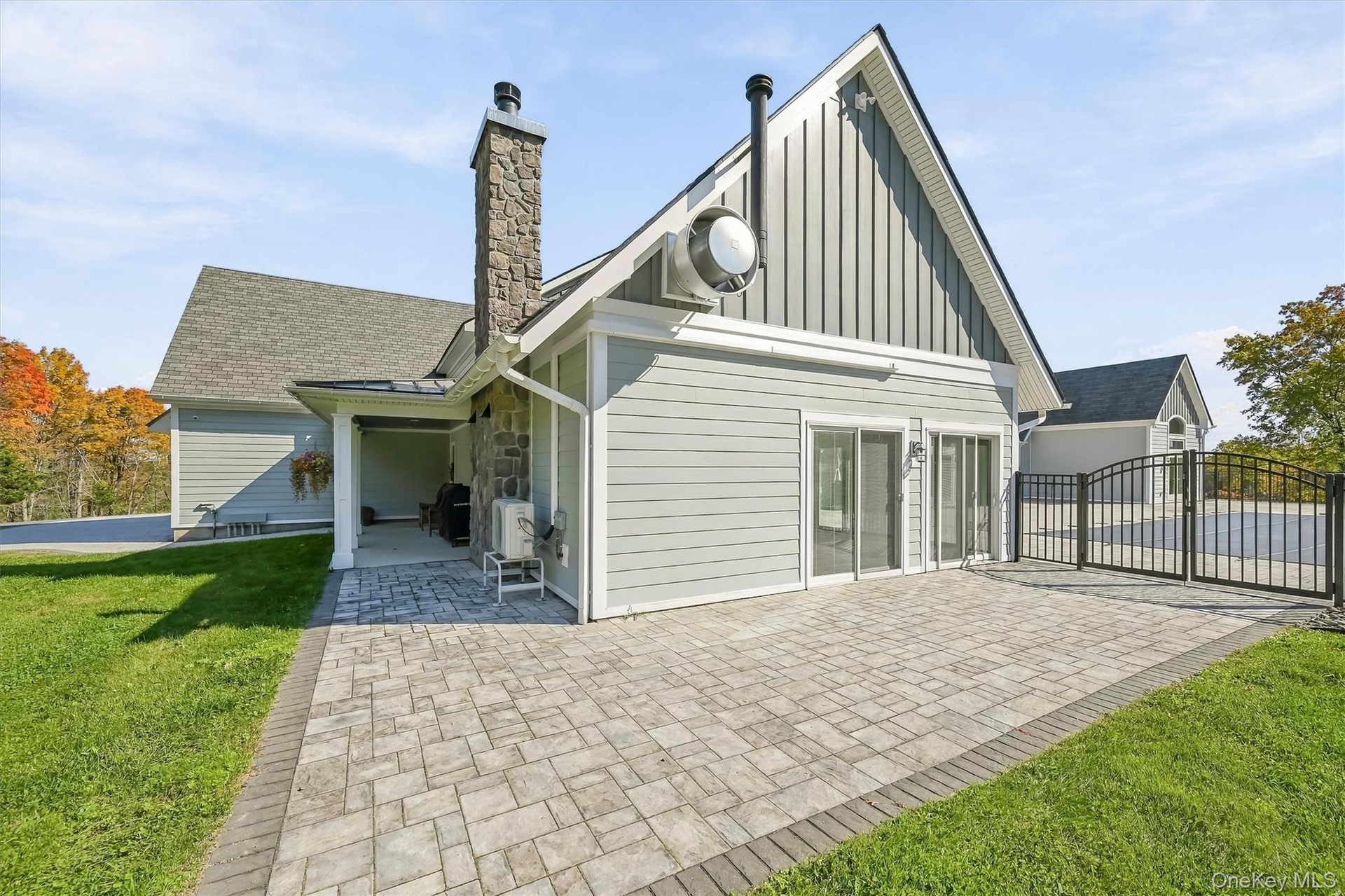 Exterior featuring a stone-clad chimney, composite siding, a paved patio, and a metal perimeter fence around the pool area