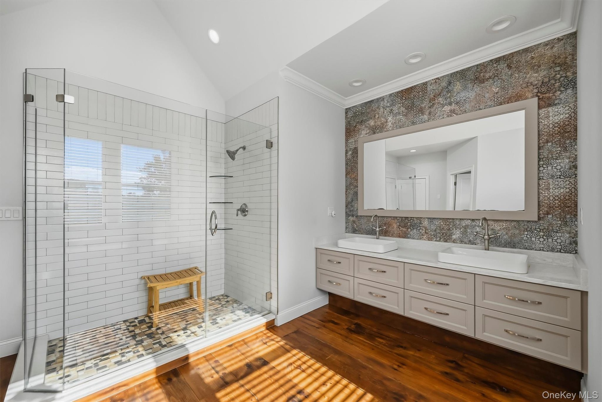Dual vanity with white vessel sinks and stone countertop, walk-in glass-enclosed shower featuring white subway tile, and wood-finish flooring