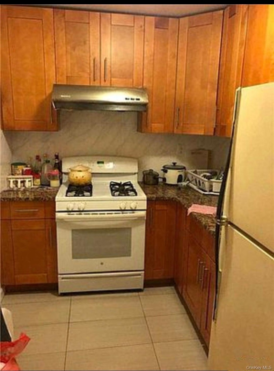 Kitchen featuring white appliances, light tile patterned flooring, brown cabinets, and under cabinet range hood