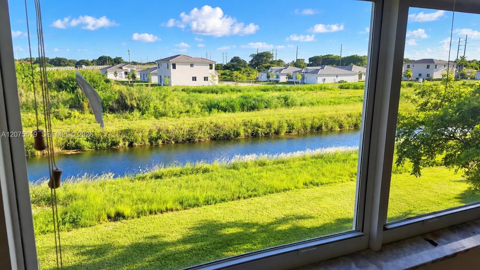 Expansive multi-pane window featuring water frontage, grassy landscape, and mature trees