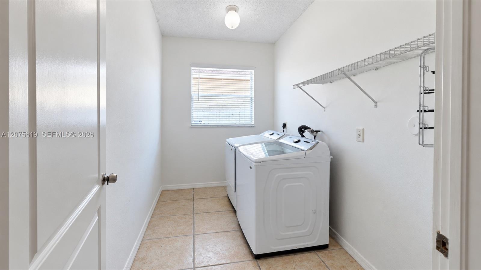 Utility room featuring tiled flooring, a single-pane window, ceiling-mounted light fixture, and built-in wire shelving