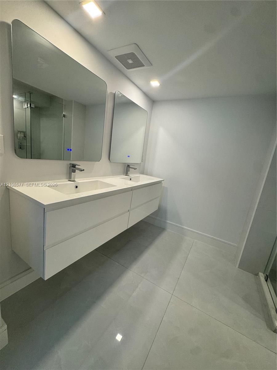 Floating double vanity with a stone countertop, integrated sinks, chrome faucets, and two illuminated mirrors, complemented by large-format tile floor
