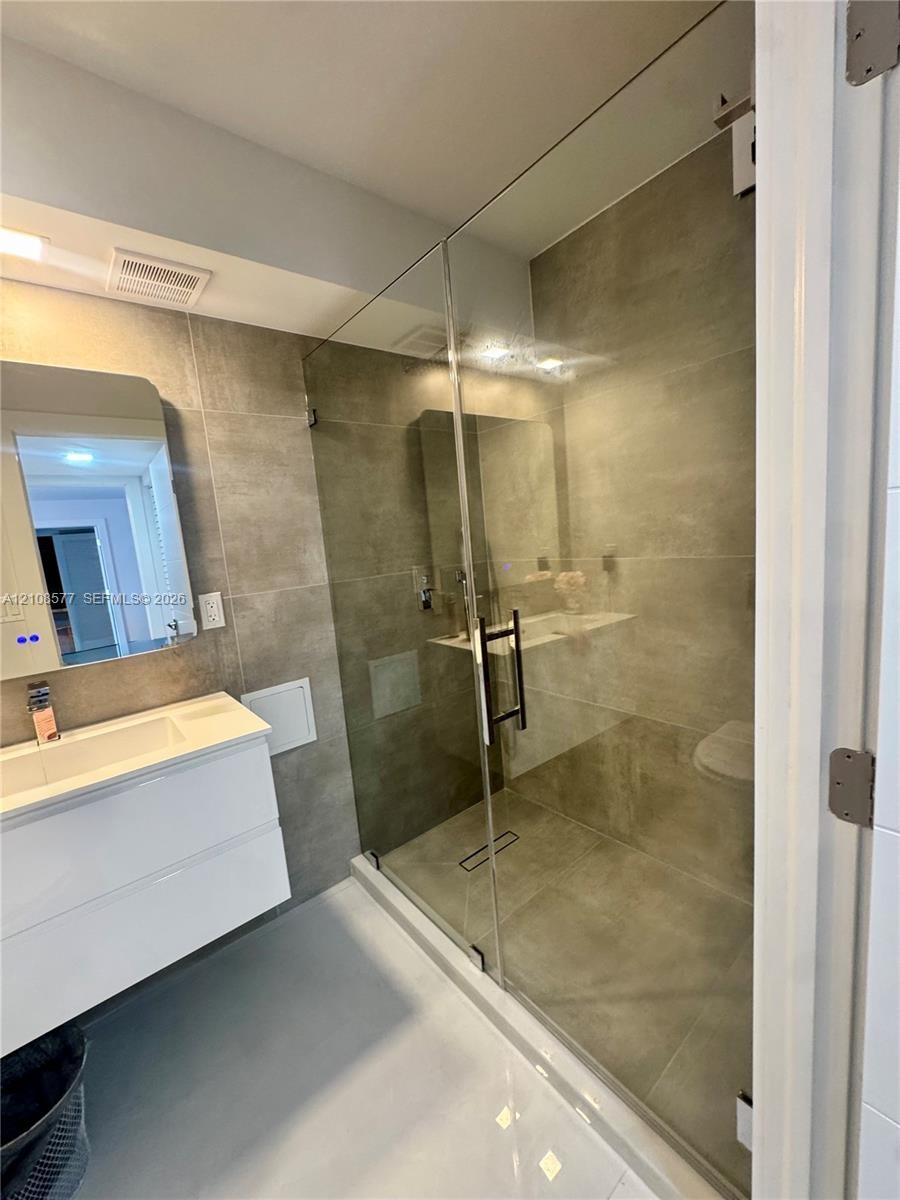 Bathroom featuring a wall-mounted floating vanity, rectangular integrated sink, glass-enclosed shower with large-format tile surround, and an illumina
