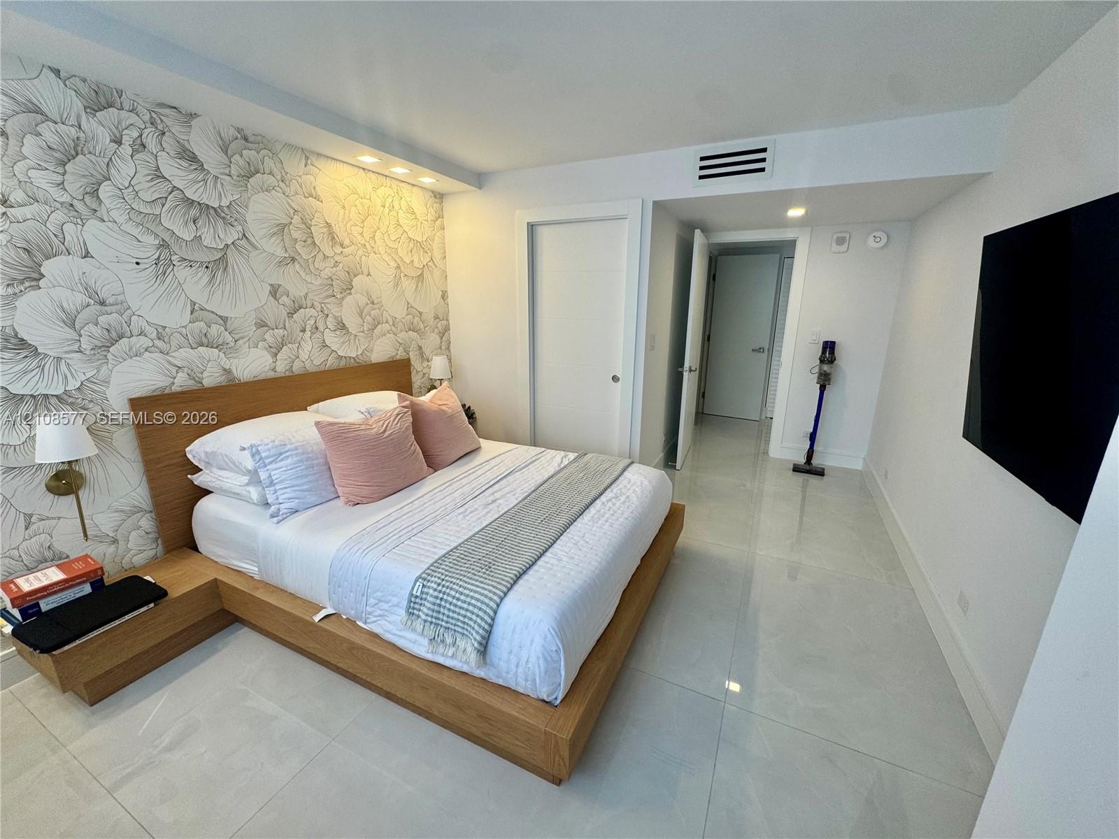 Large-format tile flooring, patterned accent wall, built-in wooden platform bed frame with integrated side tables, and recessed ceiling lighting