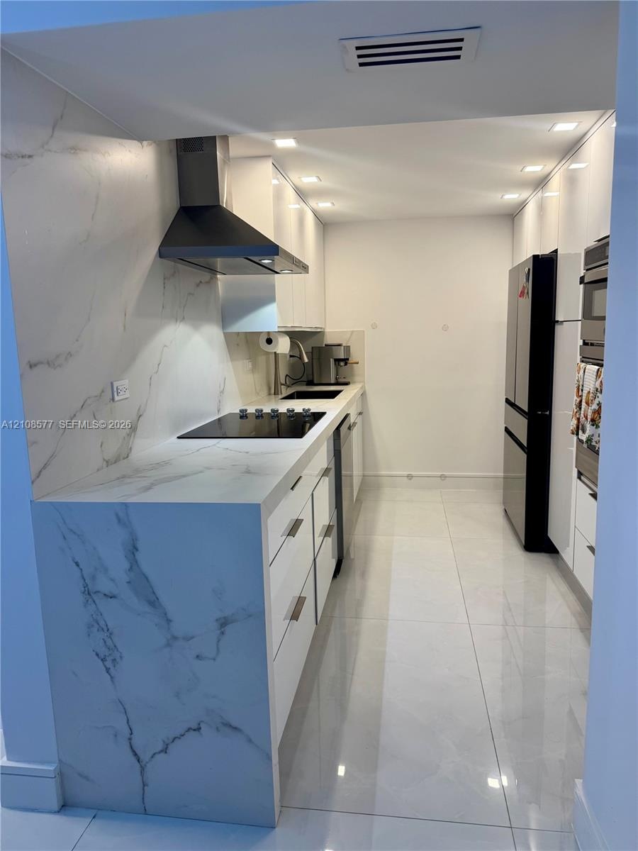 Sleek kitchen featuring high-gloss cabinetry, stone-finish countertops with matching full-height backsplash, polished tile flooring, and integrated st