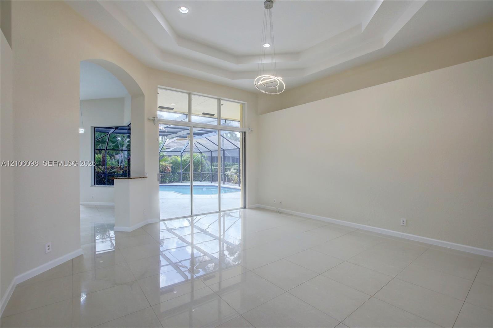 Interior space featuring tile flooring, a recessed tray ceiling, architectural archway, and expansive sliding glass doors opening to a screened pool e
