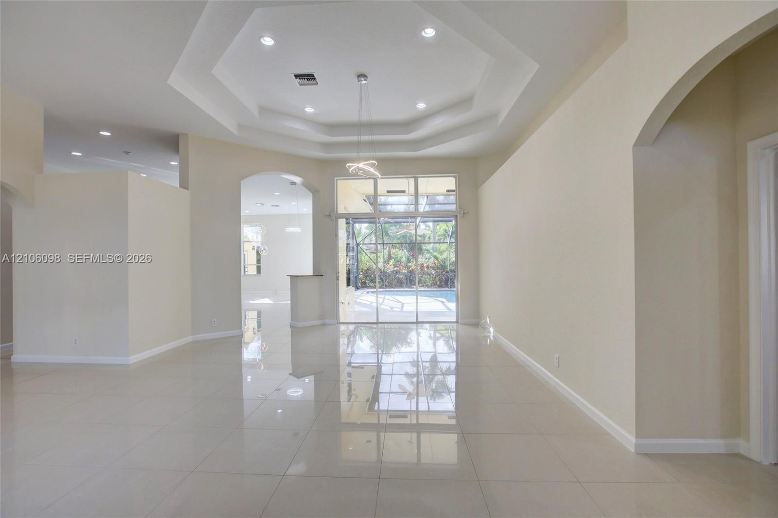 Open interior featuring polished tile flooring, tray ceilings with recessed lighting, an architectural archway, and expansive floor-to-ceiling glass p