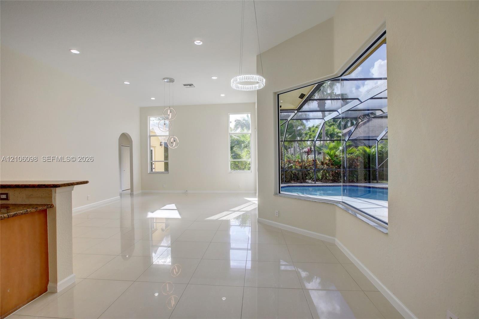 Open-concept living space featuring high ceilings, polished tile flooring, recessed lighting, and a large bay window with a screen-enclosed pool area