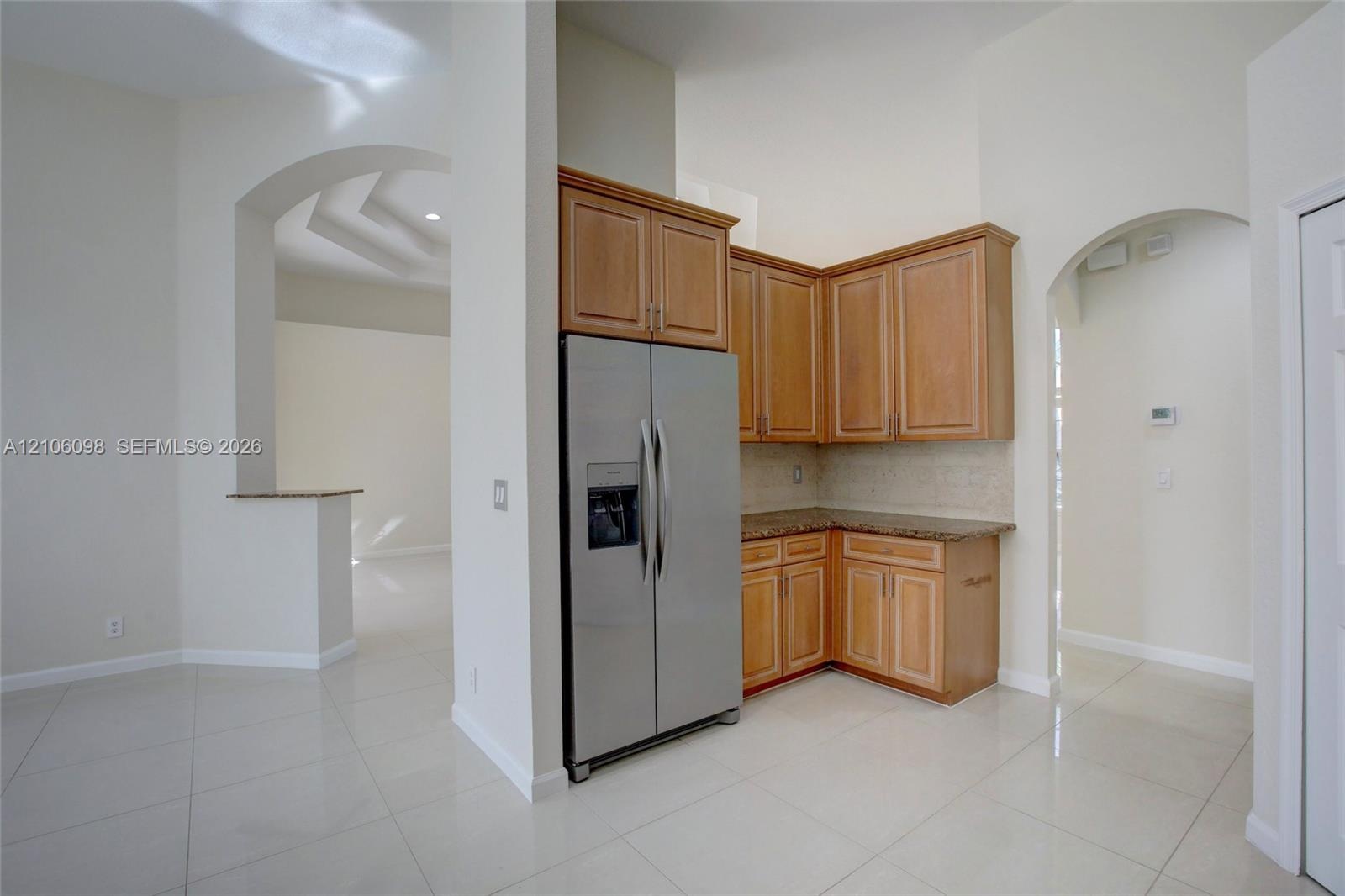 Kitchen featuring wood cabinetry, stone countertops, stainless steel side-by-side refrigerator, tile flooring, and arched architectural detailing