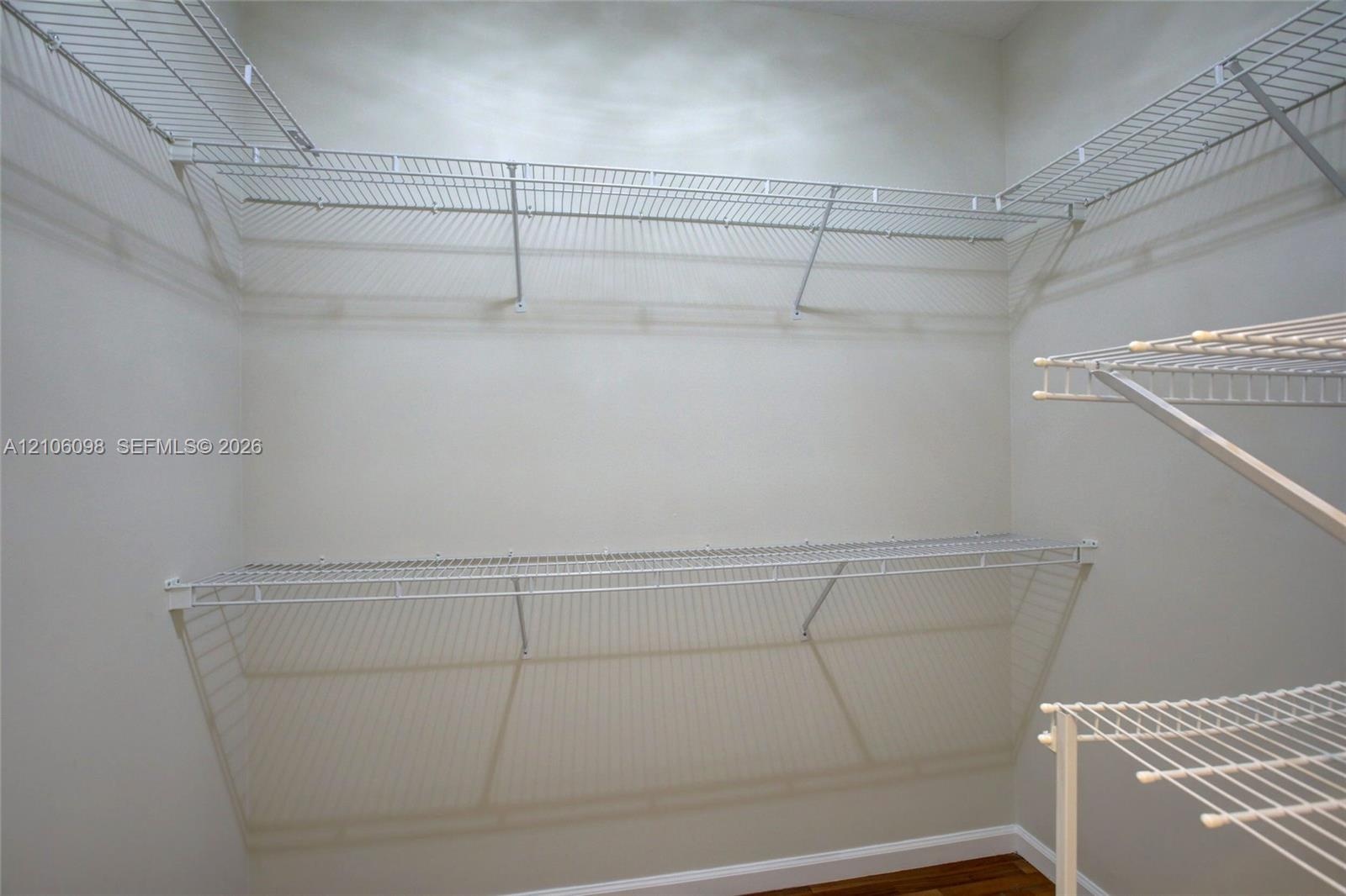 Walk-in storage space featuring multi-tiered white wire shelving and wood-finish flooring