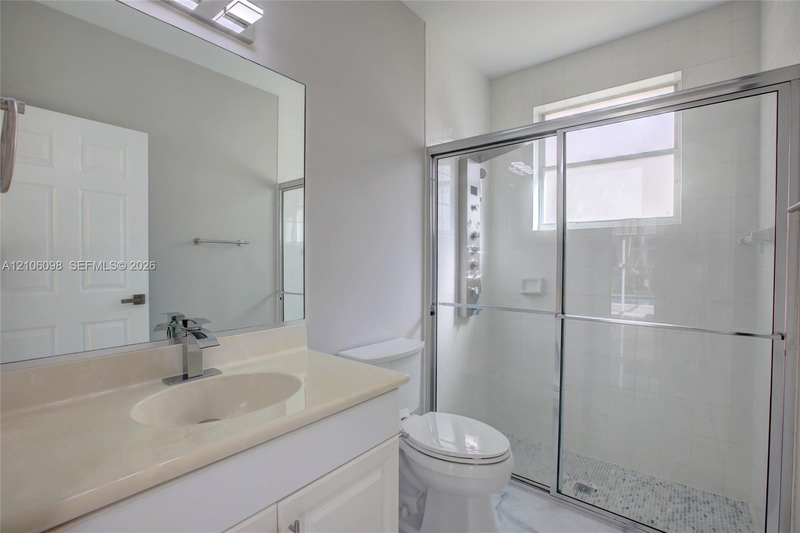 Bathroom featuring a vanity with integrated sink, large wall-mounted mirror, walk-in shower with a glass enclosure, rainfall shower panel system, and 