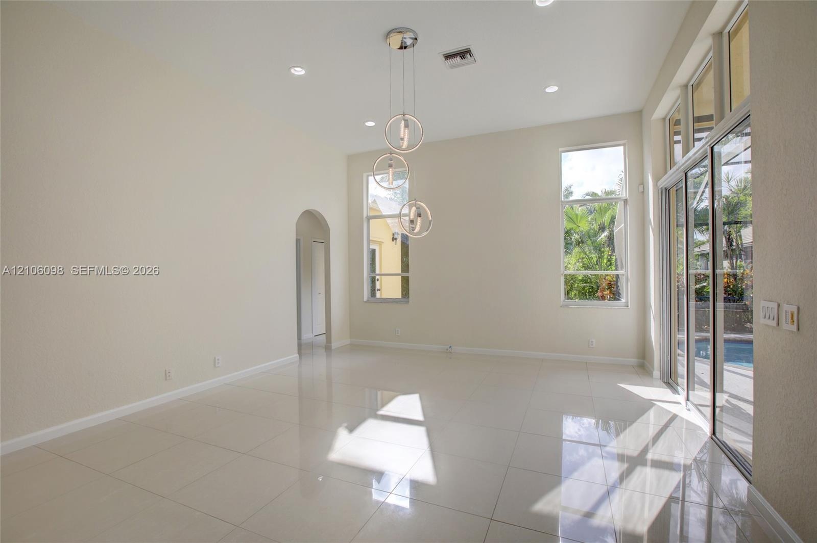 High-ceiling living area featuring large-format tile flooring, a multi-tier contemporary pendant light fixture, arched entryways, and sliding glass do