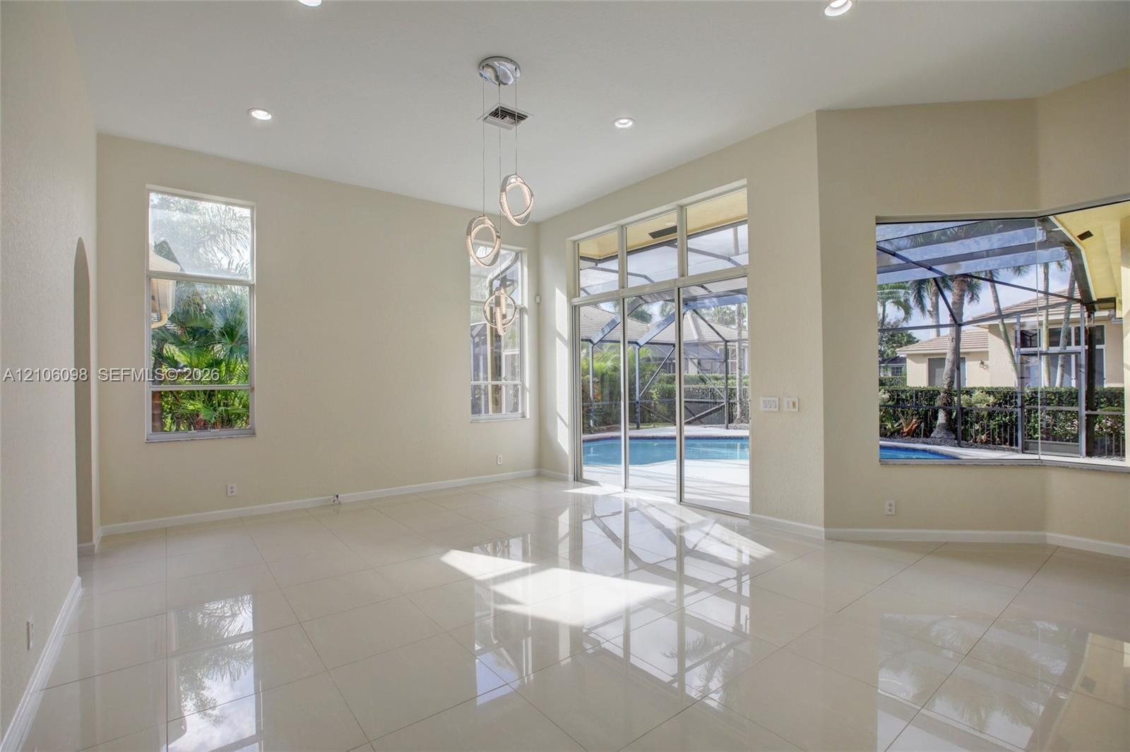 High ceilings with recessed lighting, large-format tile flooring, multi-light pendant fixture, floor-to-ceiling windows, and sliding glass doors openi