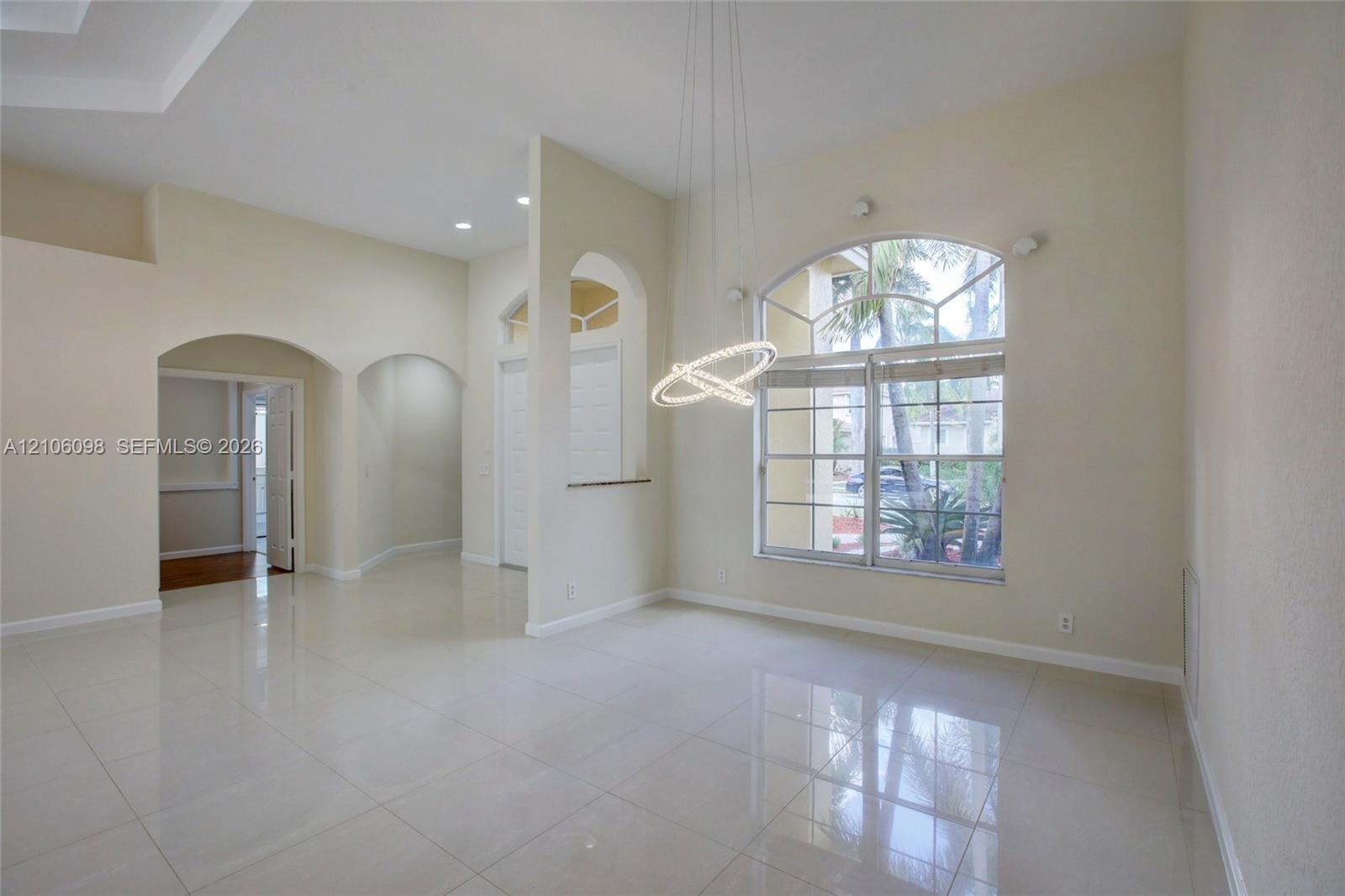 Open-concept interior featuring polished tile flooring, arched wall cutouts, a contemporary circular pendant light fixture, and a large arched multi-p