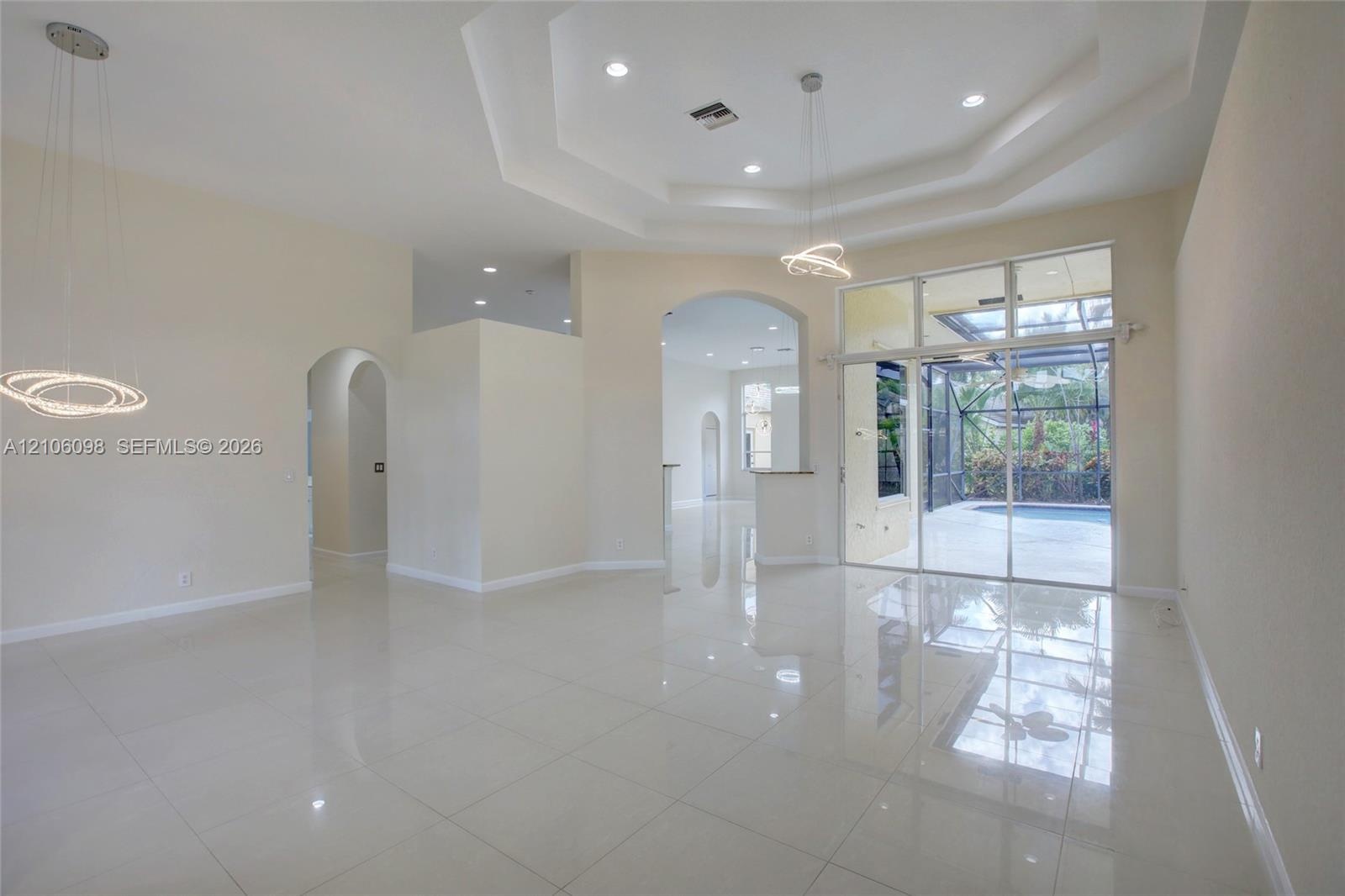 Open interior featuring a tray ceiling, recessed lighting, modern geometric pendant light fixtures, light-toned tile flooring, and floor-to-ceiling gl