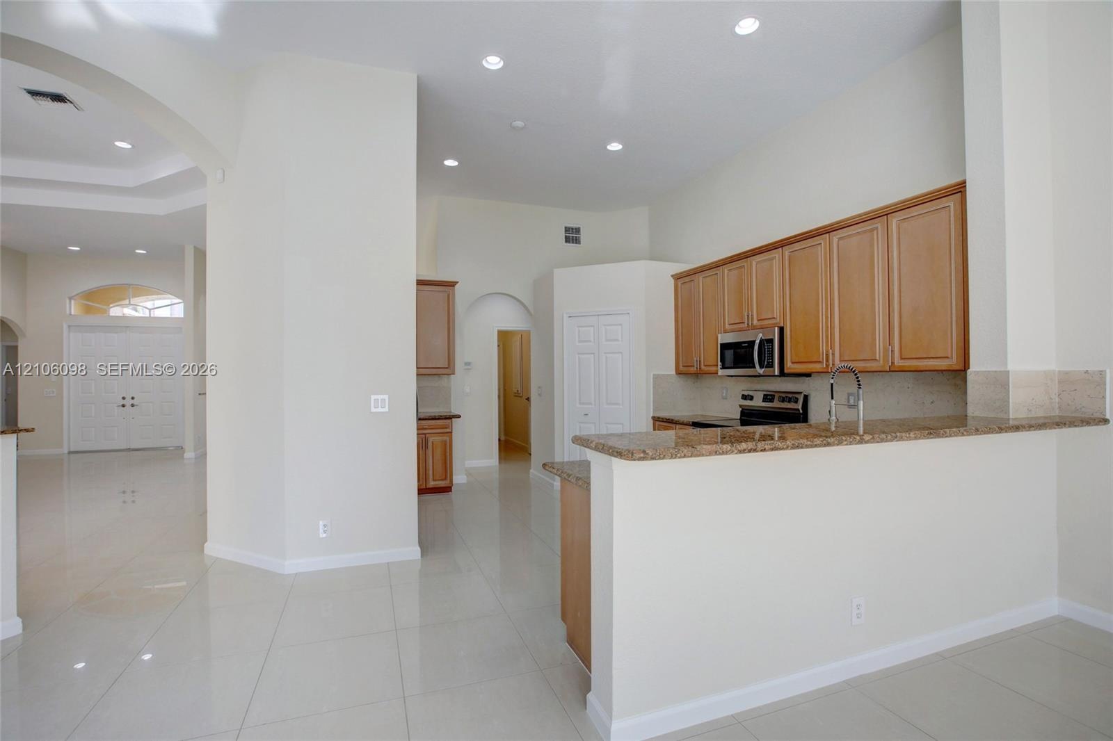 Kitchen featuring stone countertops, natural wood-finish cabinetry, built-in stainless steel appliances, recessed ceiling lighting, and tile flooring 
