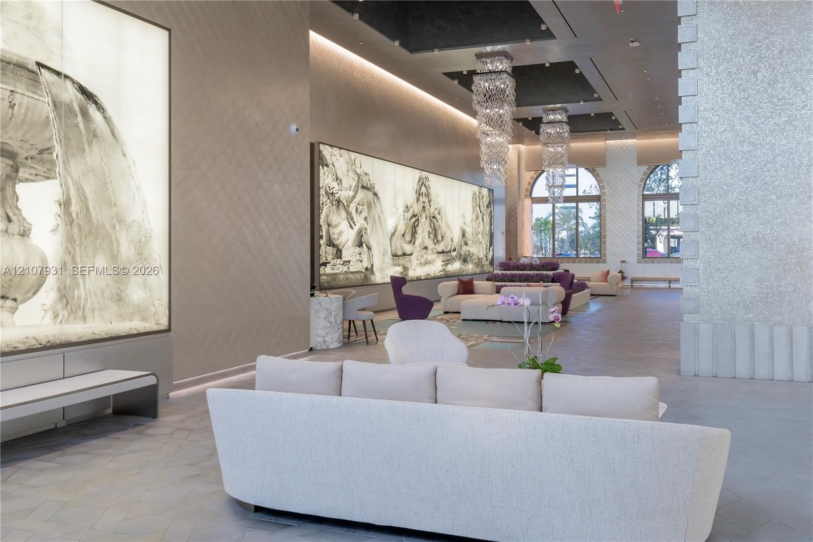 Grand foyer featuring high ceilings with recessed lighting, tiered crystal chandeliers, large-format mural wall installations, arched windows, and her