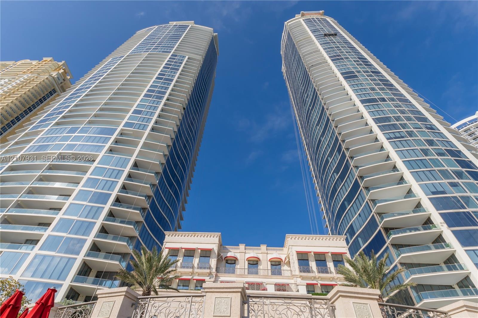 High-rise towers featuring glass-curtain facades, tiered balconies, and an ornamental stone-finish podium base with decorative metal railings