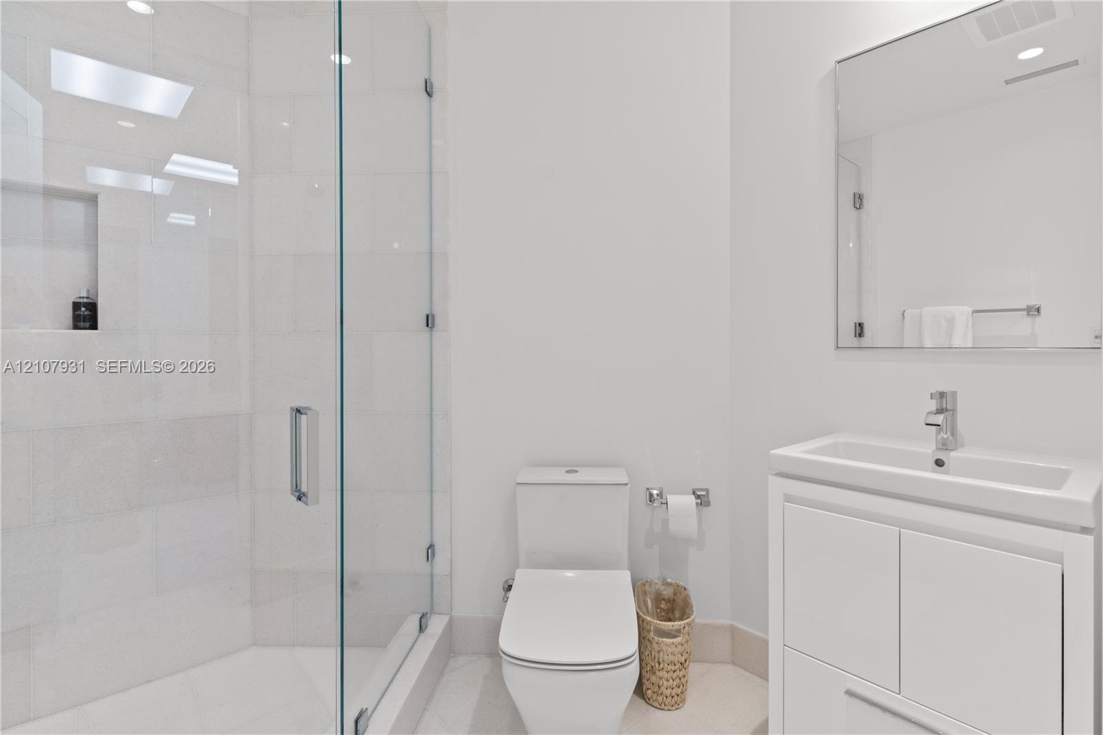 Bathroom featuring a walk-in shower with glass enclosure and tiled walls, built-in shower niche, floating-style vanity with rectangular sink, and wall