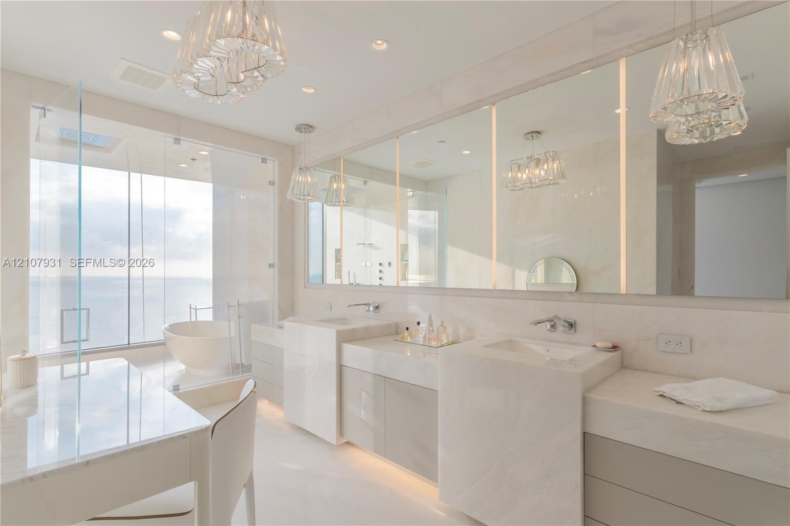 Dual-vanity cabinetry with stone-finish countertops, integrated soaking tub behind floor-to-ceiling glass, expansive wall-to-wall mirror, and tiered g
