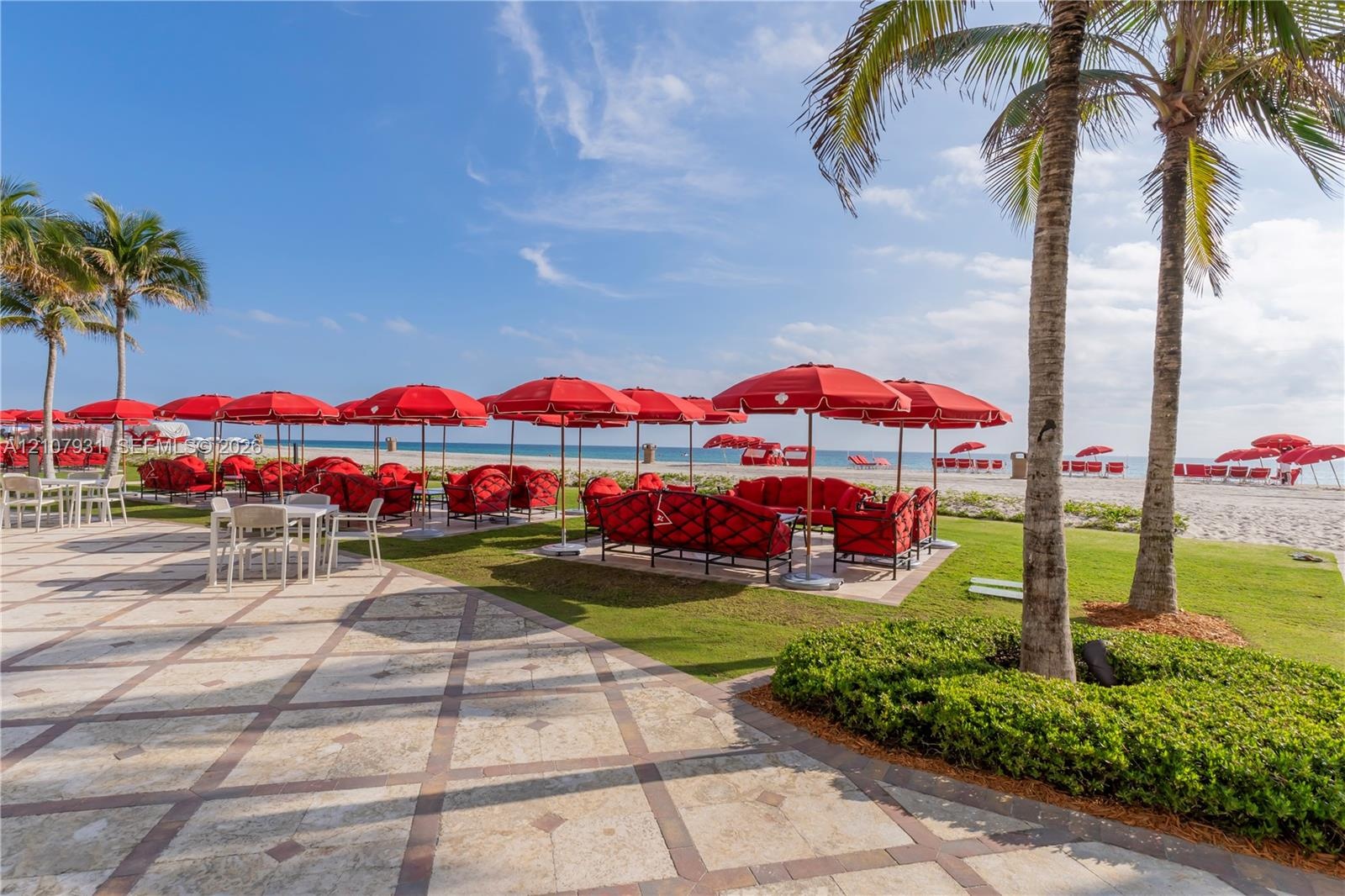 Stone paver terrace featuring manicured lawn, established palm trees, and direct oceanfront access