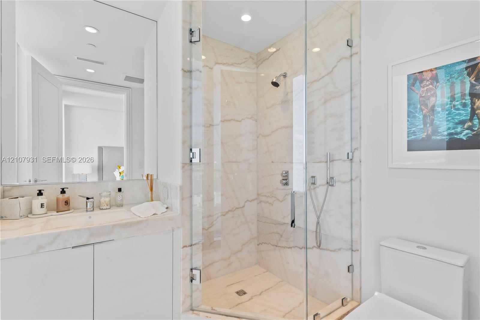 Bathroom featuring a vanity with integrated sink and stone countertop, frameless glass-enclosed shower with stone-surround, wall-to-wall mirror, and r