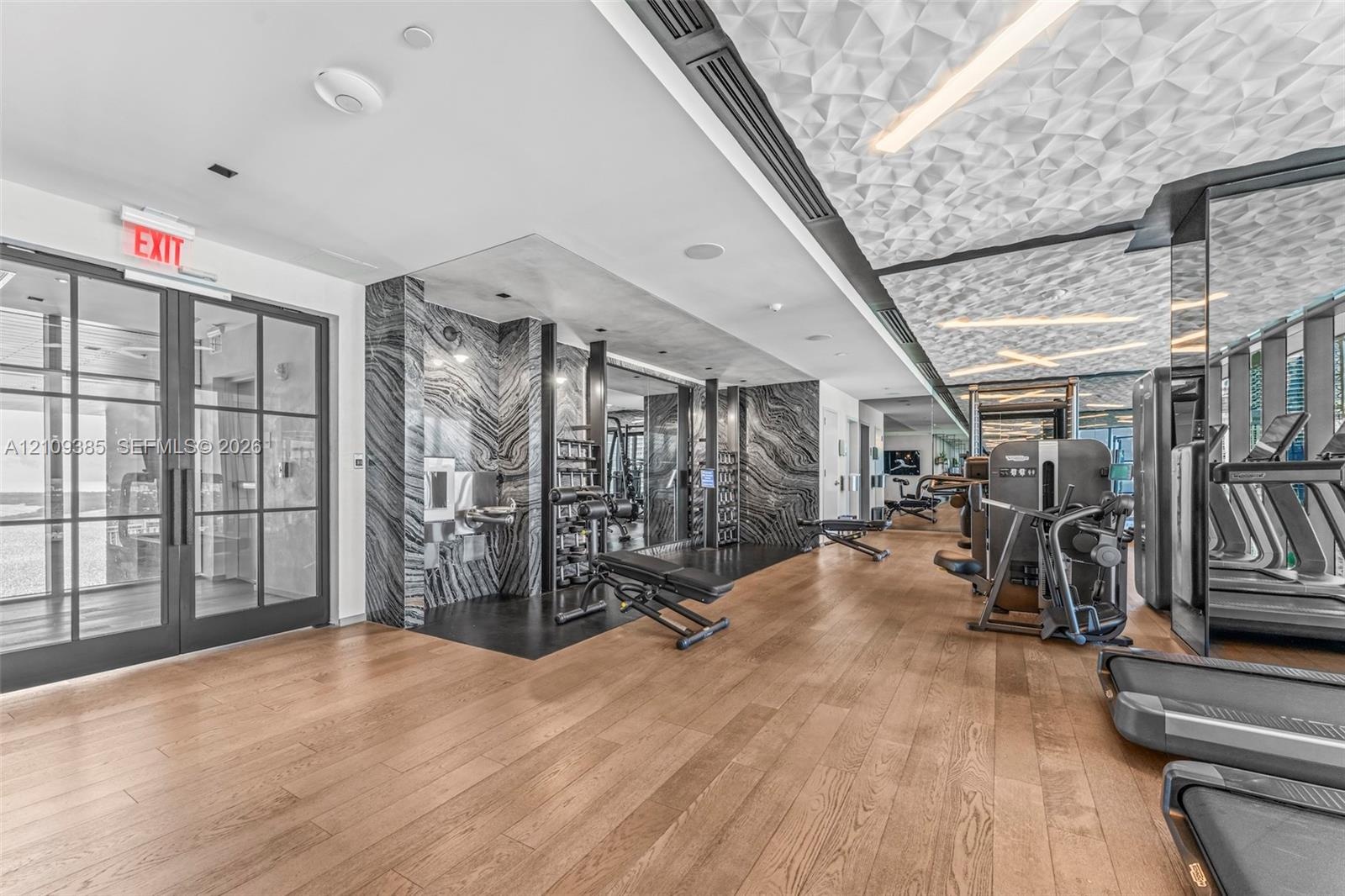 Fitness area featuring wood-finish flooring, floor-to-ceiling black-and-white stone wall cladding, a textured geometric ceiling, and double-paned glas