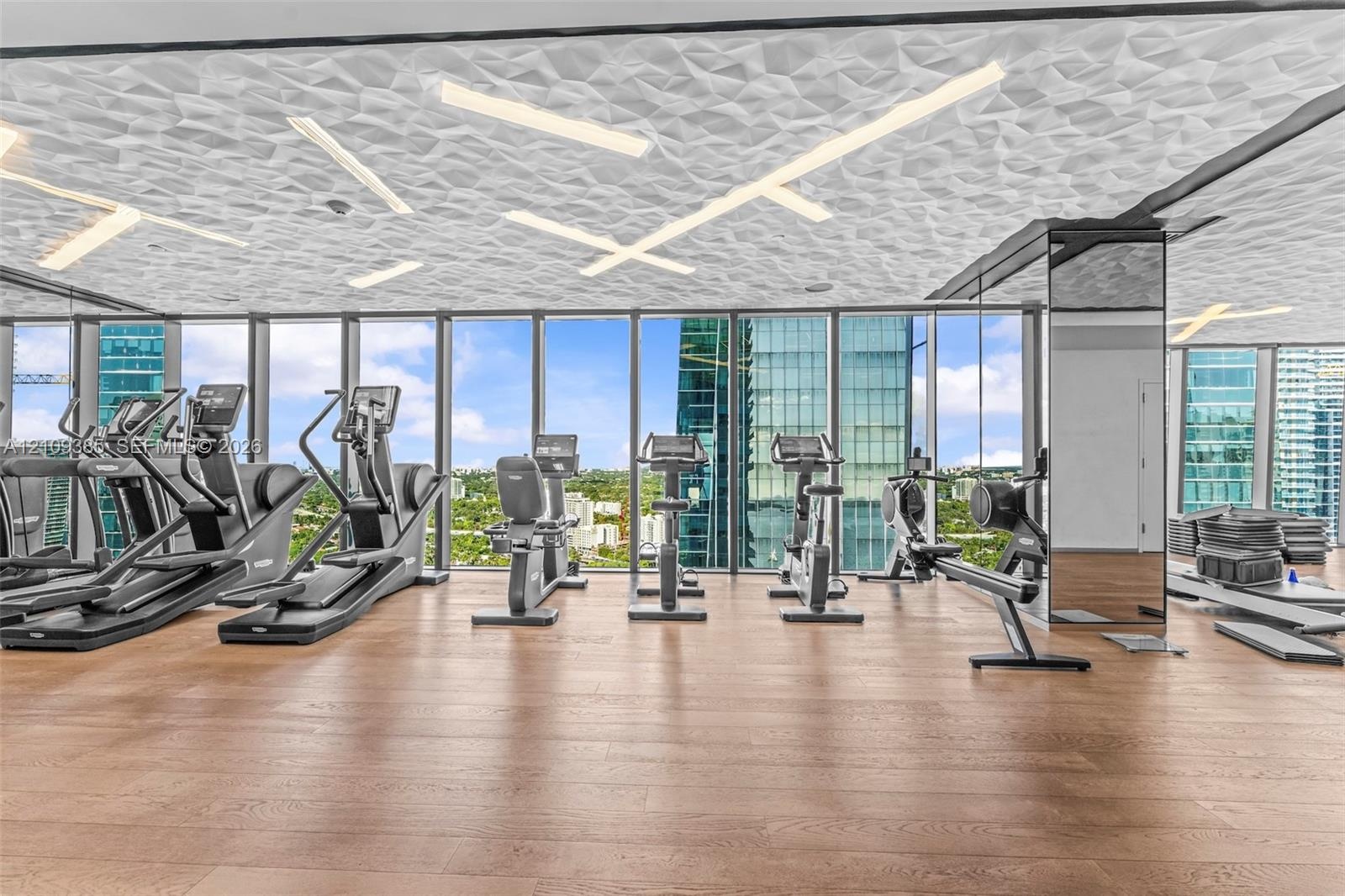Fitness center featuring wood-finish flooring, floor-to-ceiling windows, and a geometric textured ceiling with integrated linear lighting