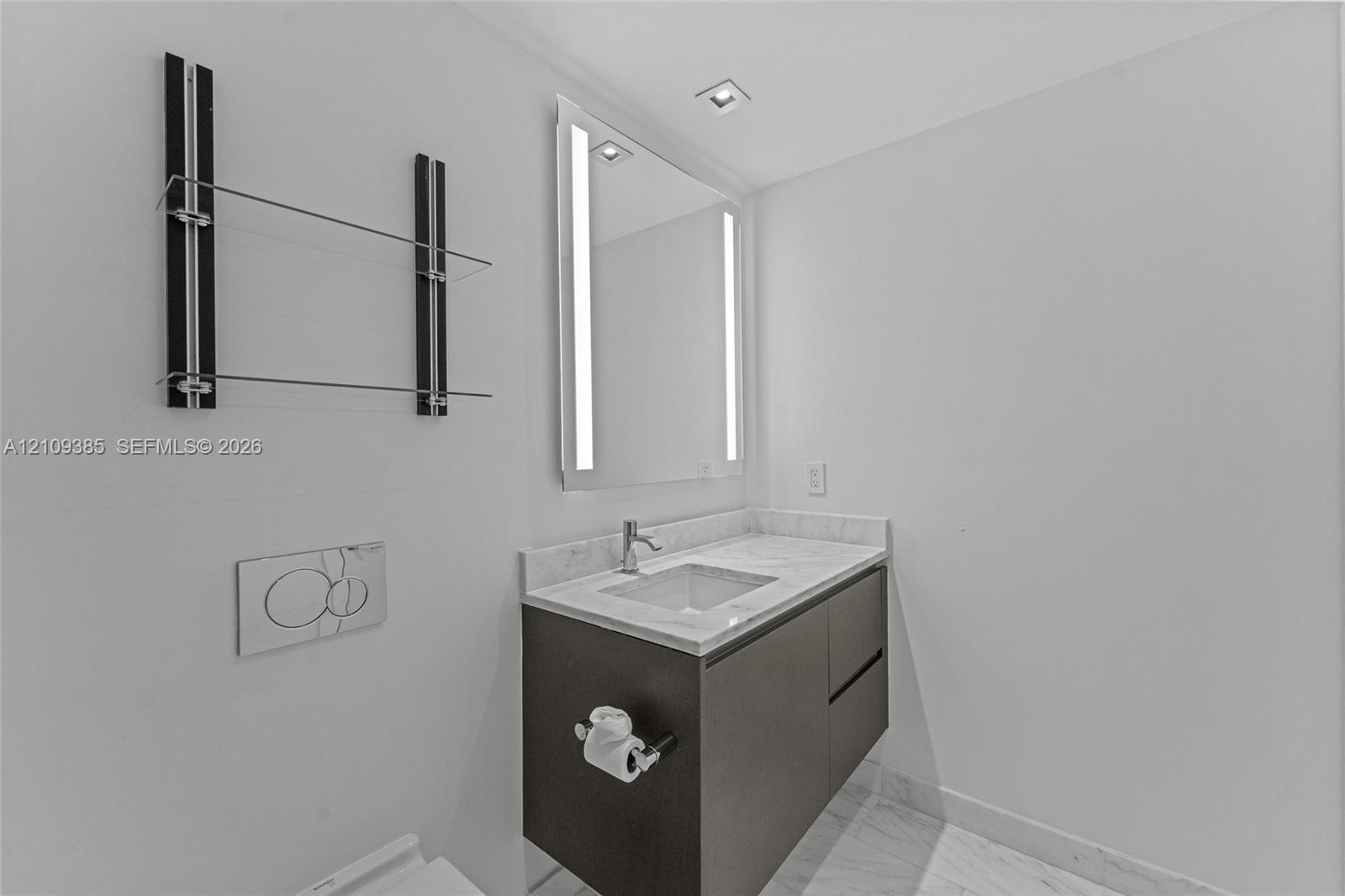 Wall-mounted dark wood-finish vanity with stone countertop, integrated sink, LED-lit mirror, built-in glass shelving, and wall-mounted dual-flush actu