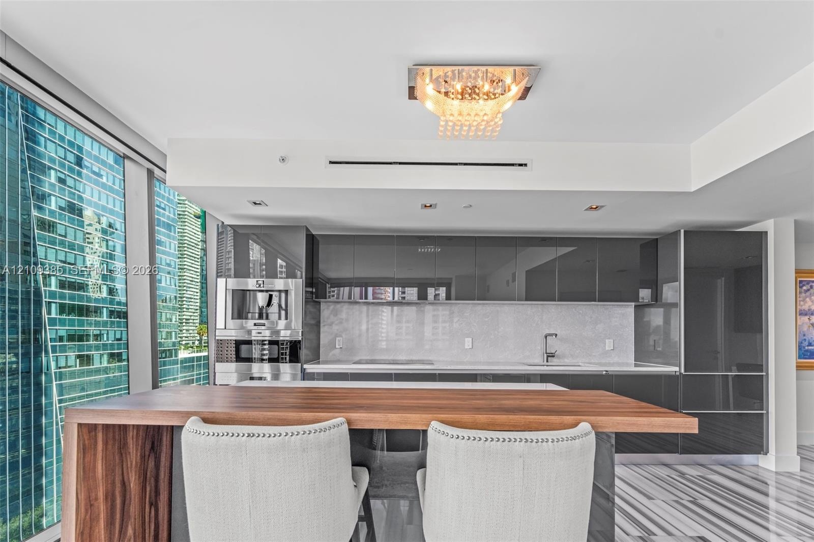 Contemporary kitchen featuring high-gloss cabinetry, stone backsplash, integrated stainless steel coffee system, wood-finish breakfast bar, and polish
